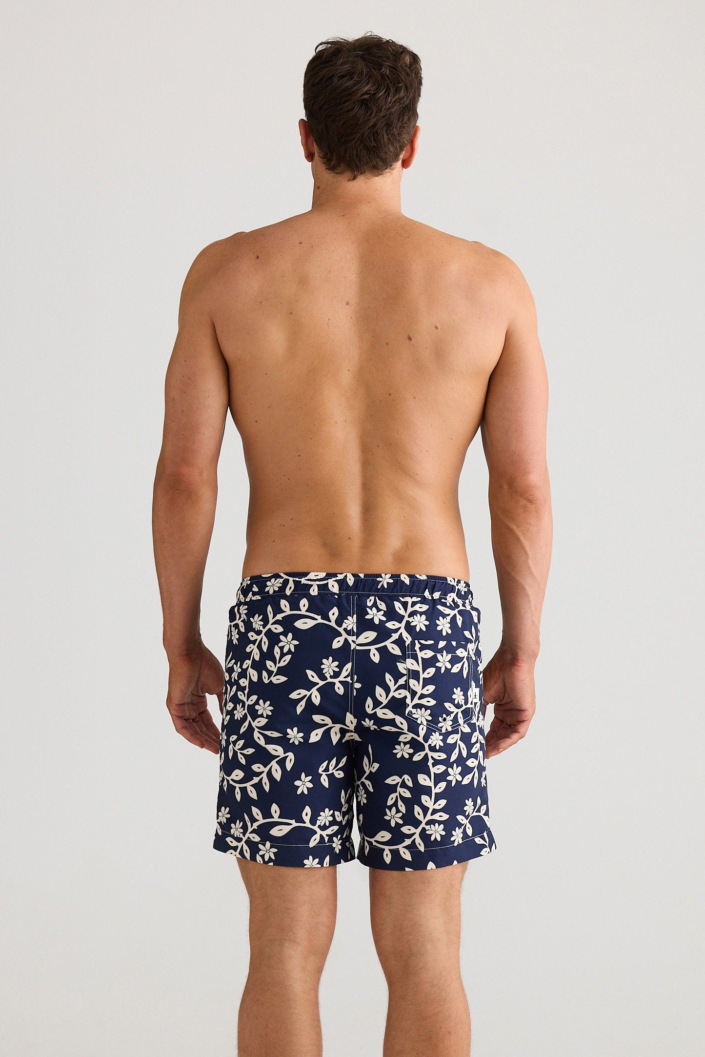 Man wearing navy blue swim shorts with a white floral pattern on a plain background