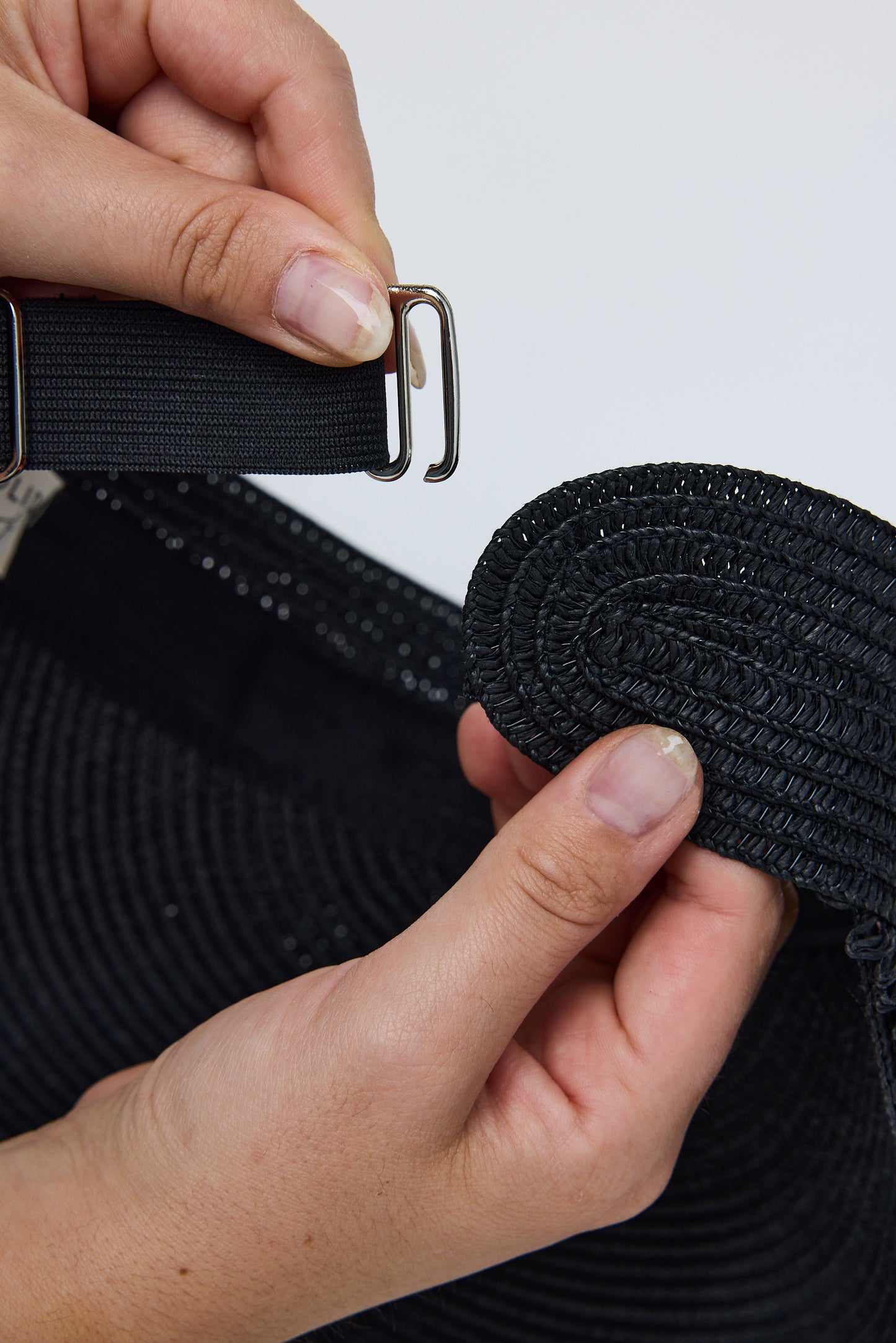 Close-up of hands holding a black belt with a metal buckle against a white background