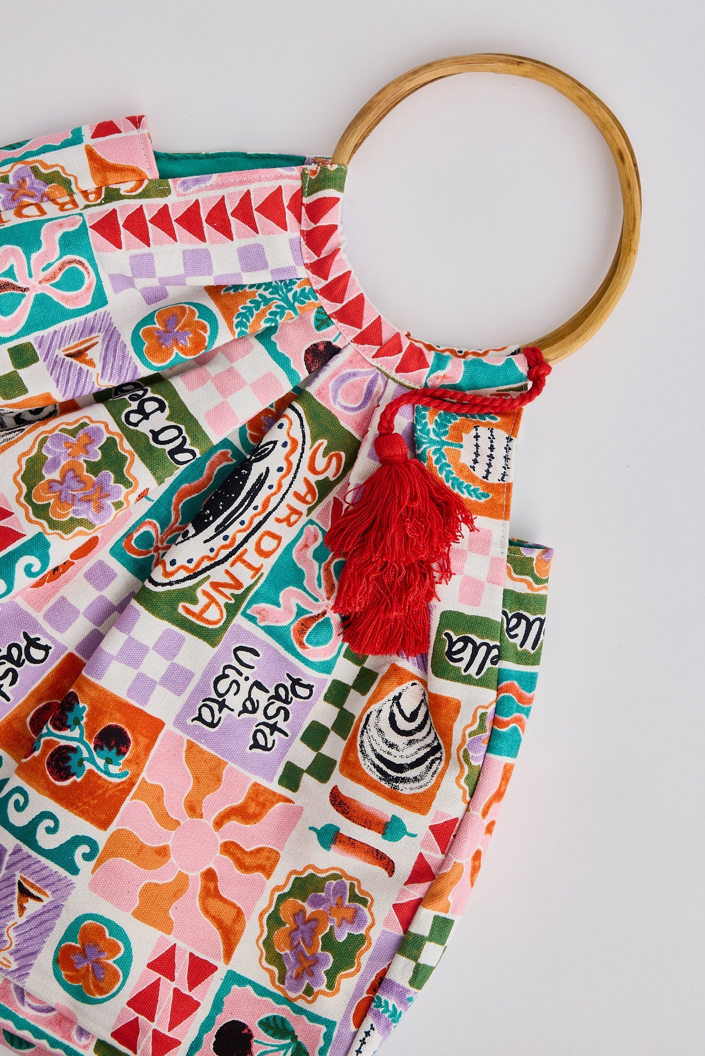 Colorful patterned bag with a wooden handle and red tassel on a light gray background