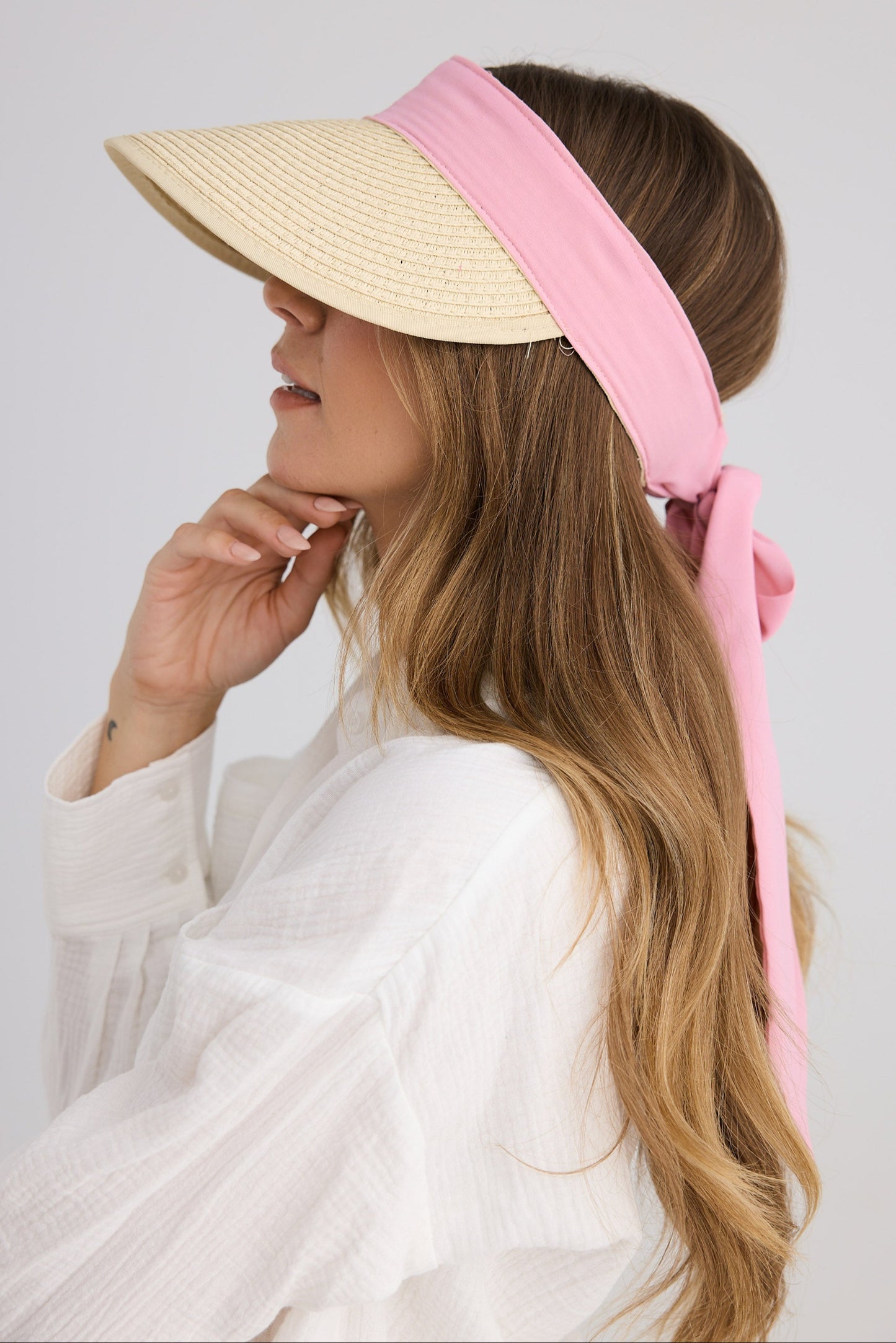 Woman wearing a beige sun visor with a pink ribbon on a plain background