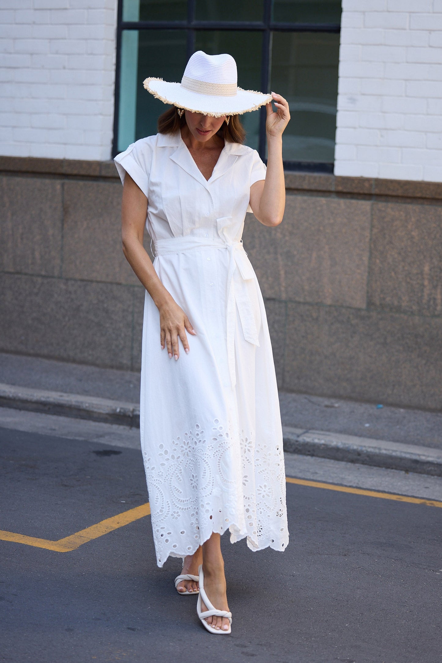 Woman in a white dress and hat walking on a street.