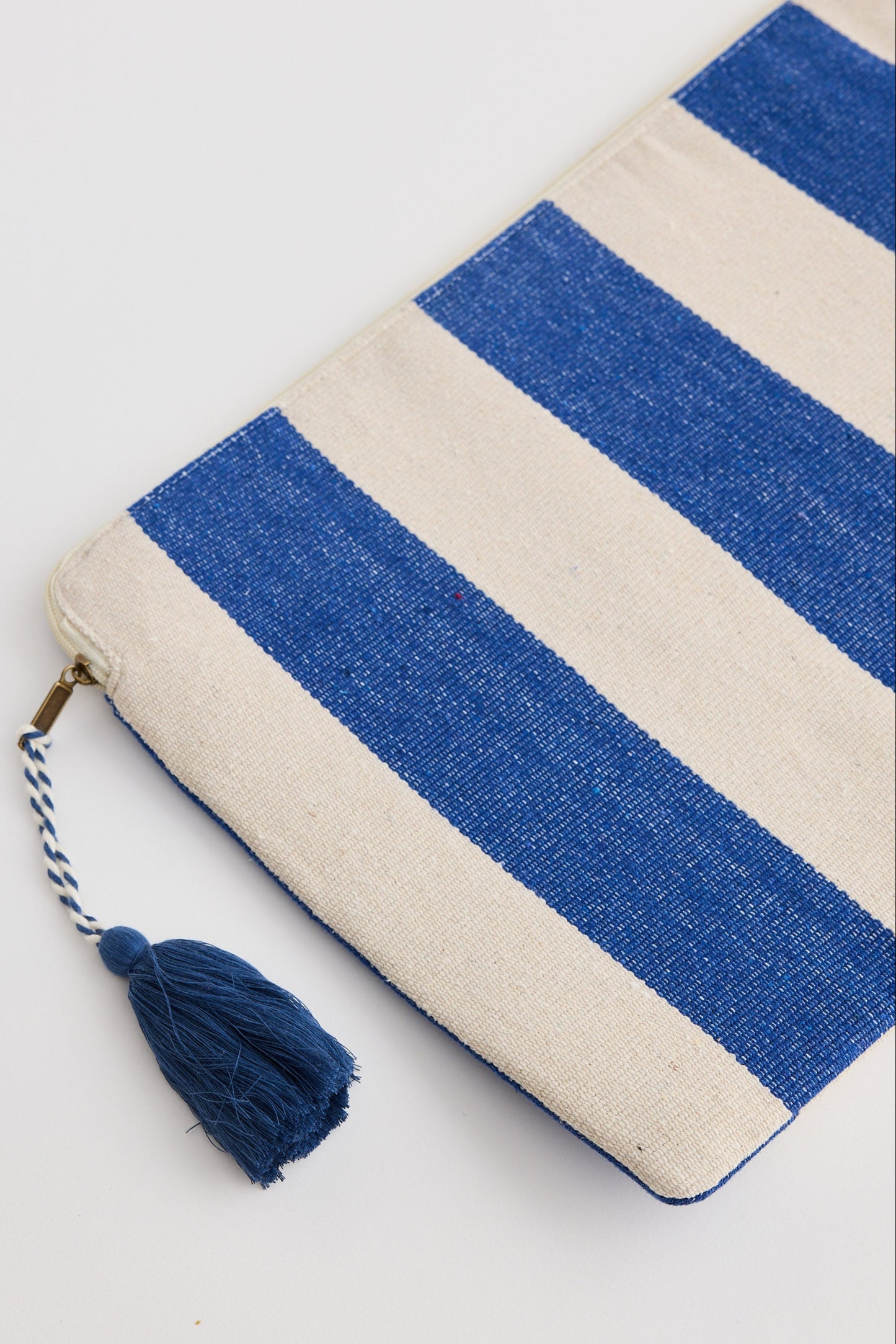 Blue and beige striped pouch with a tassel on a light gray background