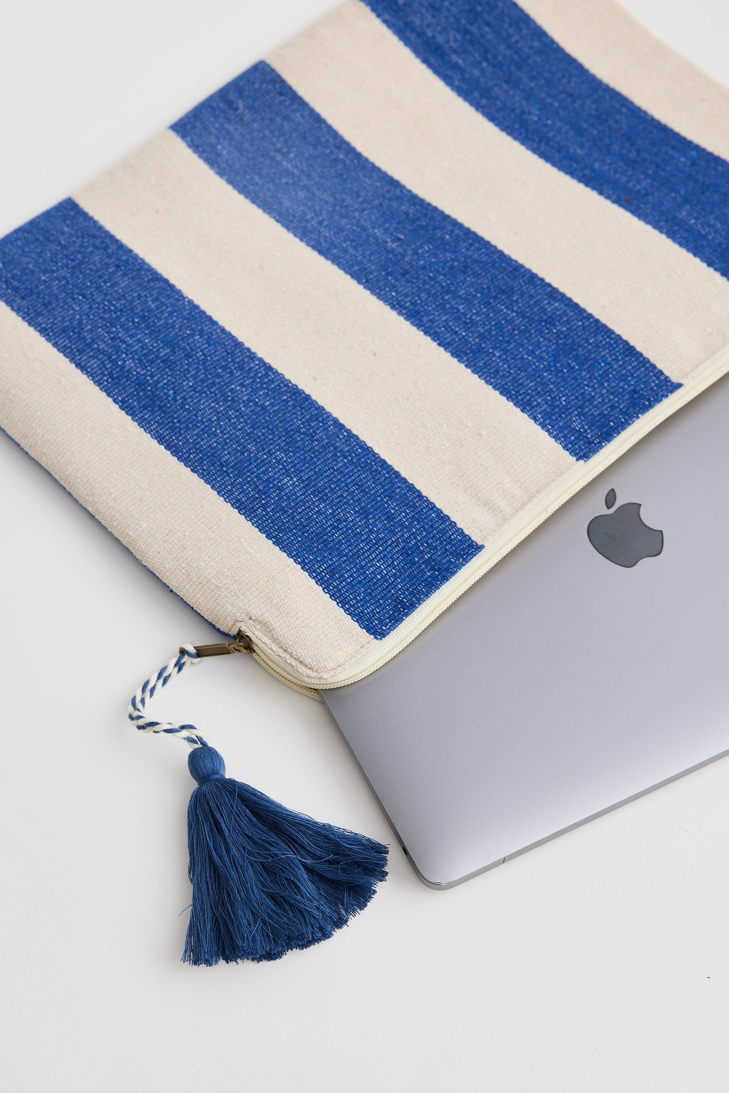 Laptop with a blue and beige striped cover and tassel on a white surface