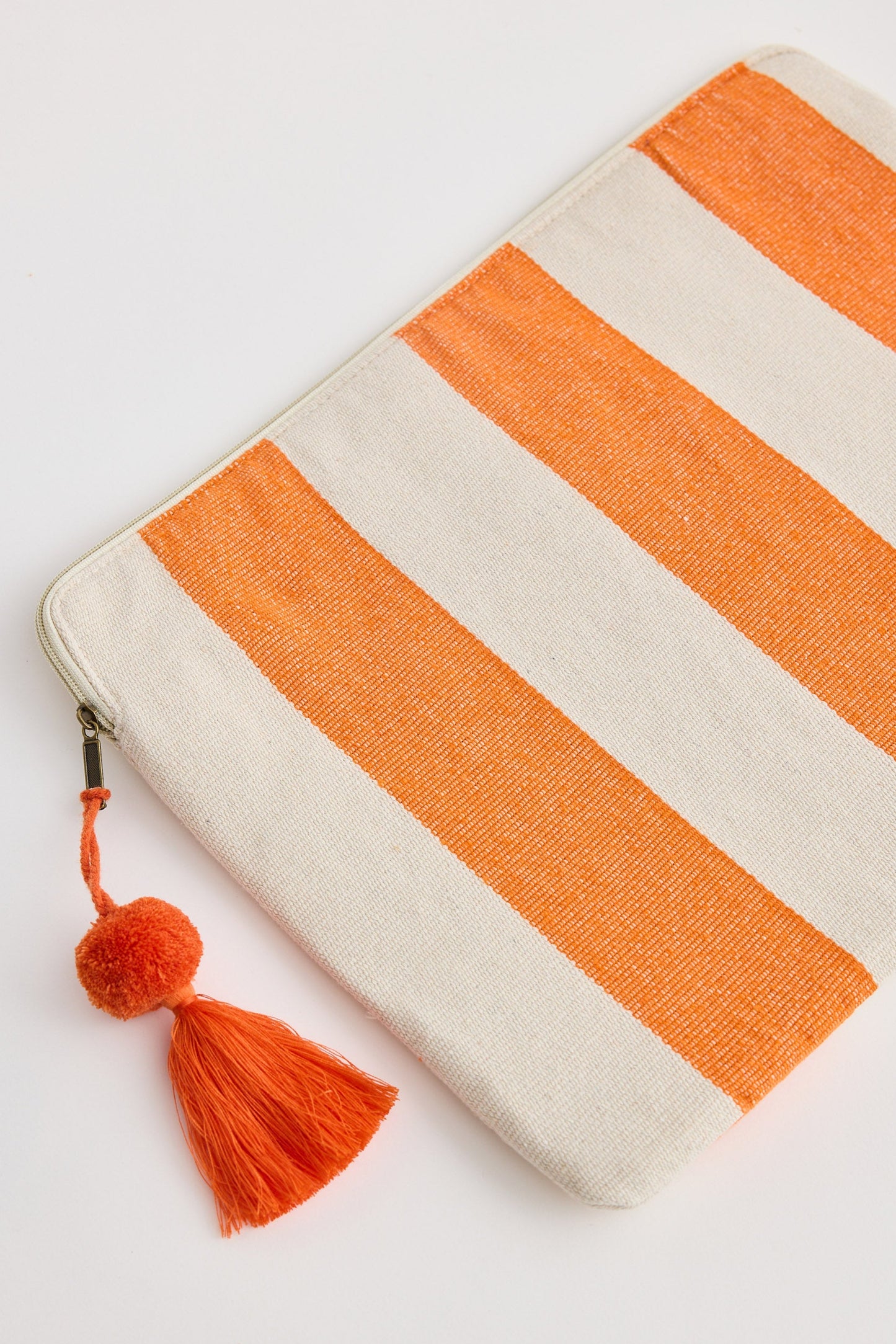 Striped pouch with orange and white pattern and tassel on a light gray background