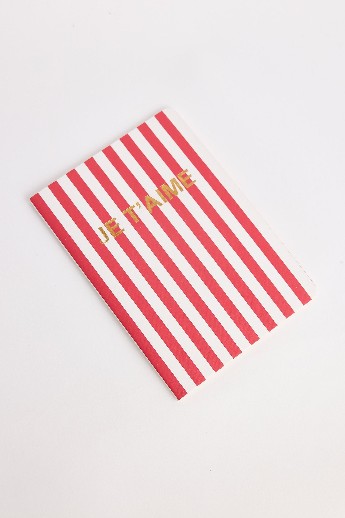 Red and white striped notebook with 'Je t'aime' text on a light gray background