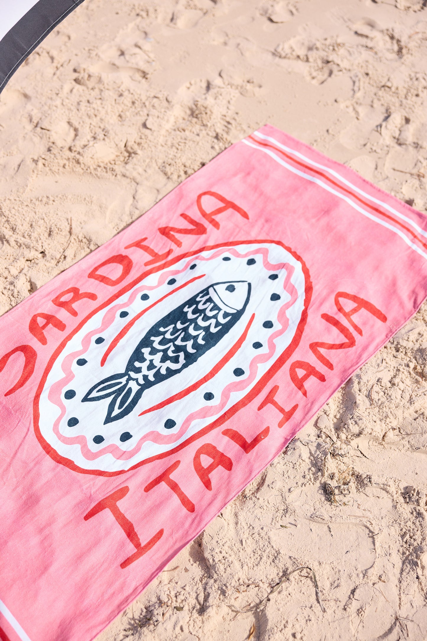Pink beach towel with fish design and text on sand