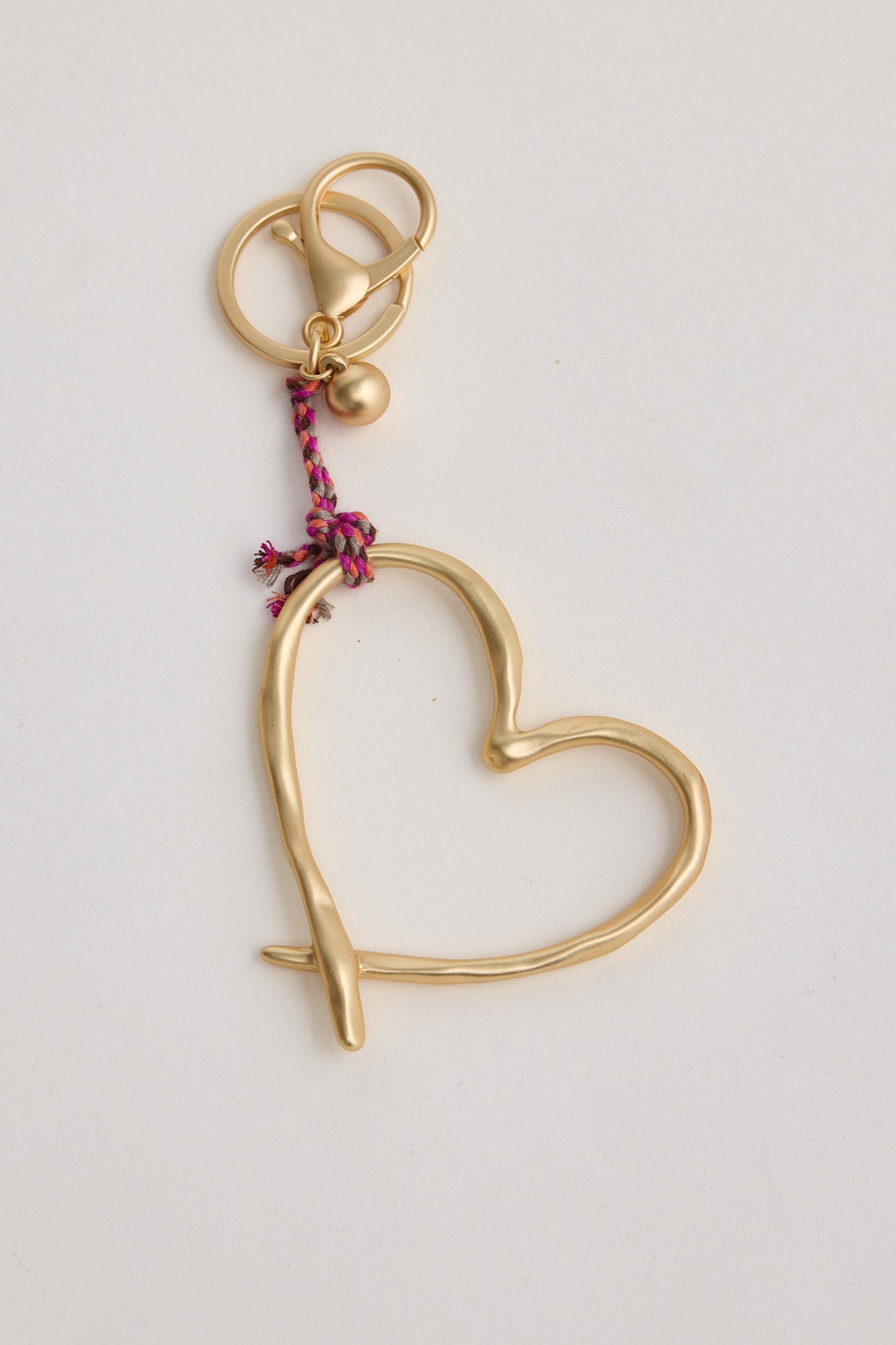Gold heart-shaped keychain with a pink string on a light gray background