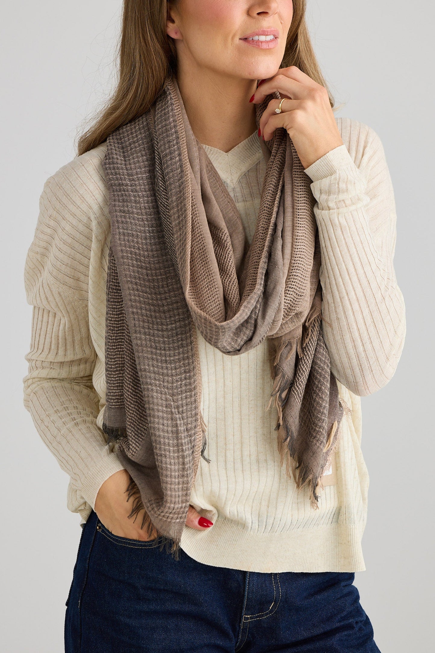 Woman wearing a beige sweater and grey scarf against a plain background