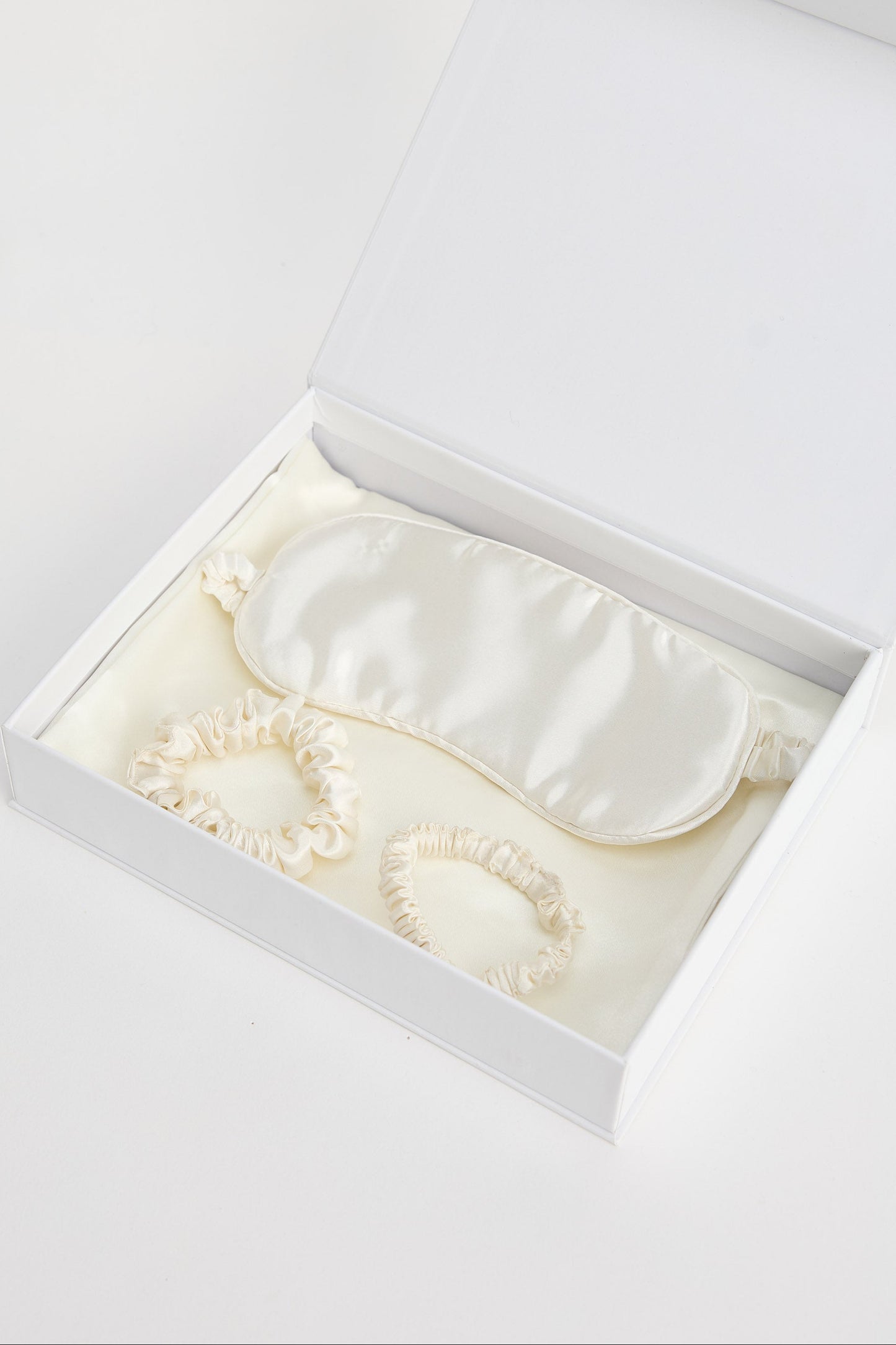 White satin eye mask in an open white box on a light gray background