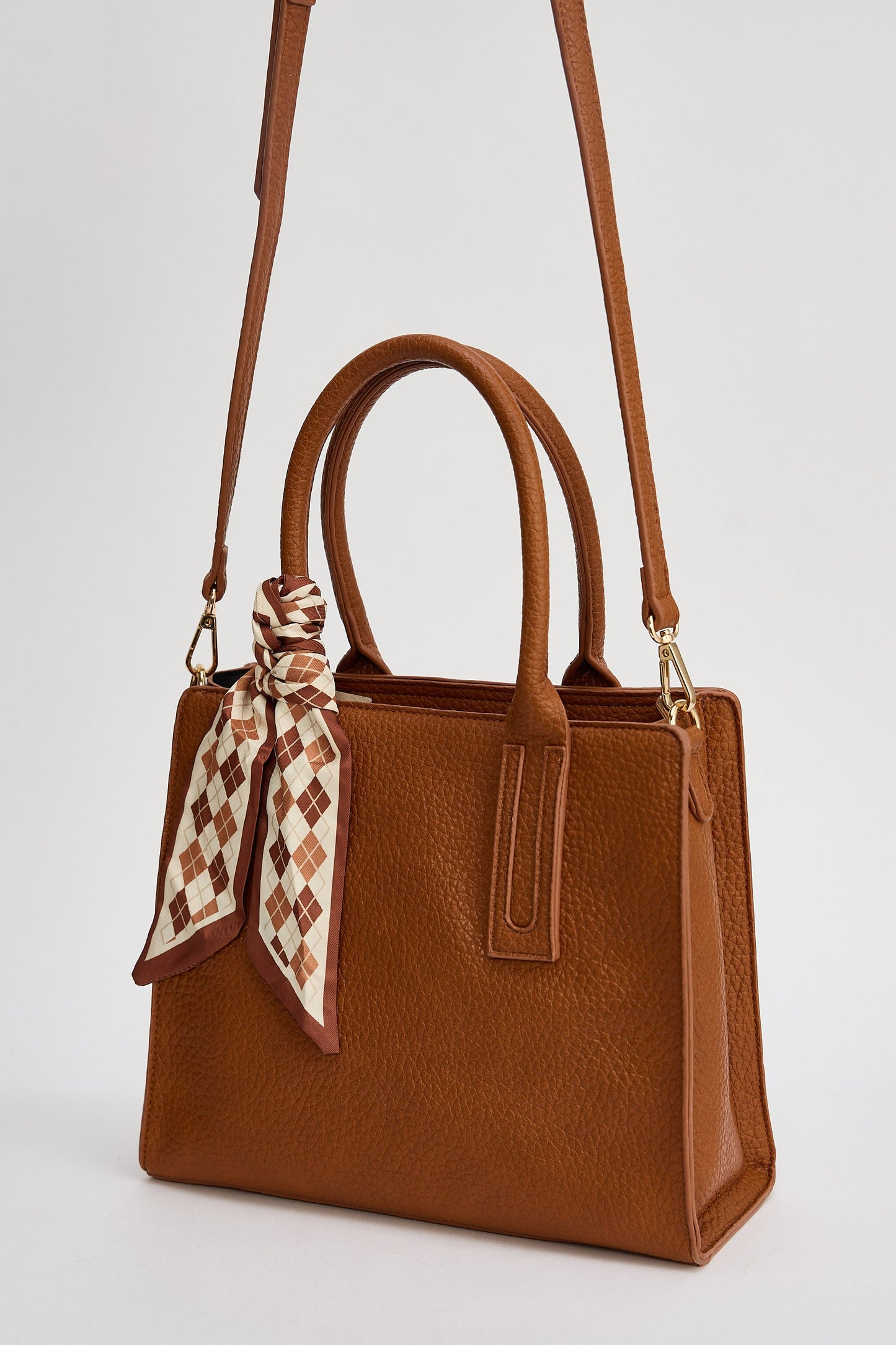 Brown handbag with a patterned scarf on a light gray background