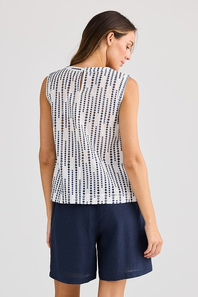 Woman wearing a sleeveless patterned top and navy shorts on a light gray background