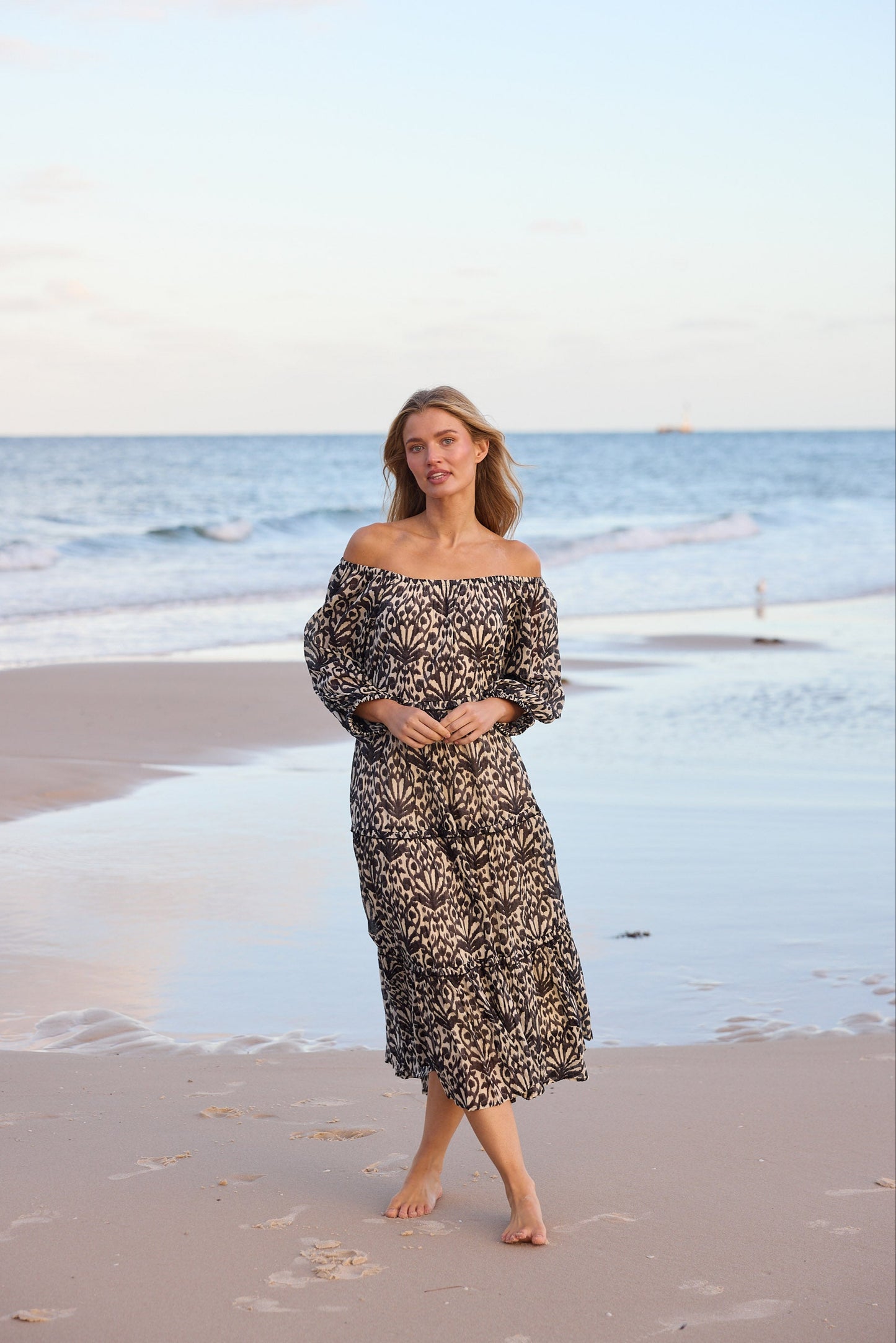 Woman in a floral dress standing on a beach with ocean and sky in the background