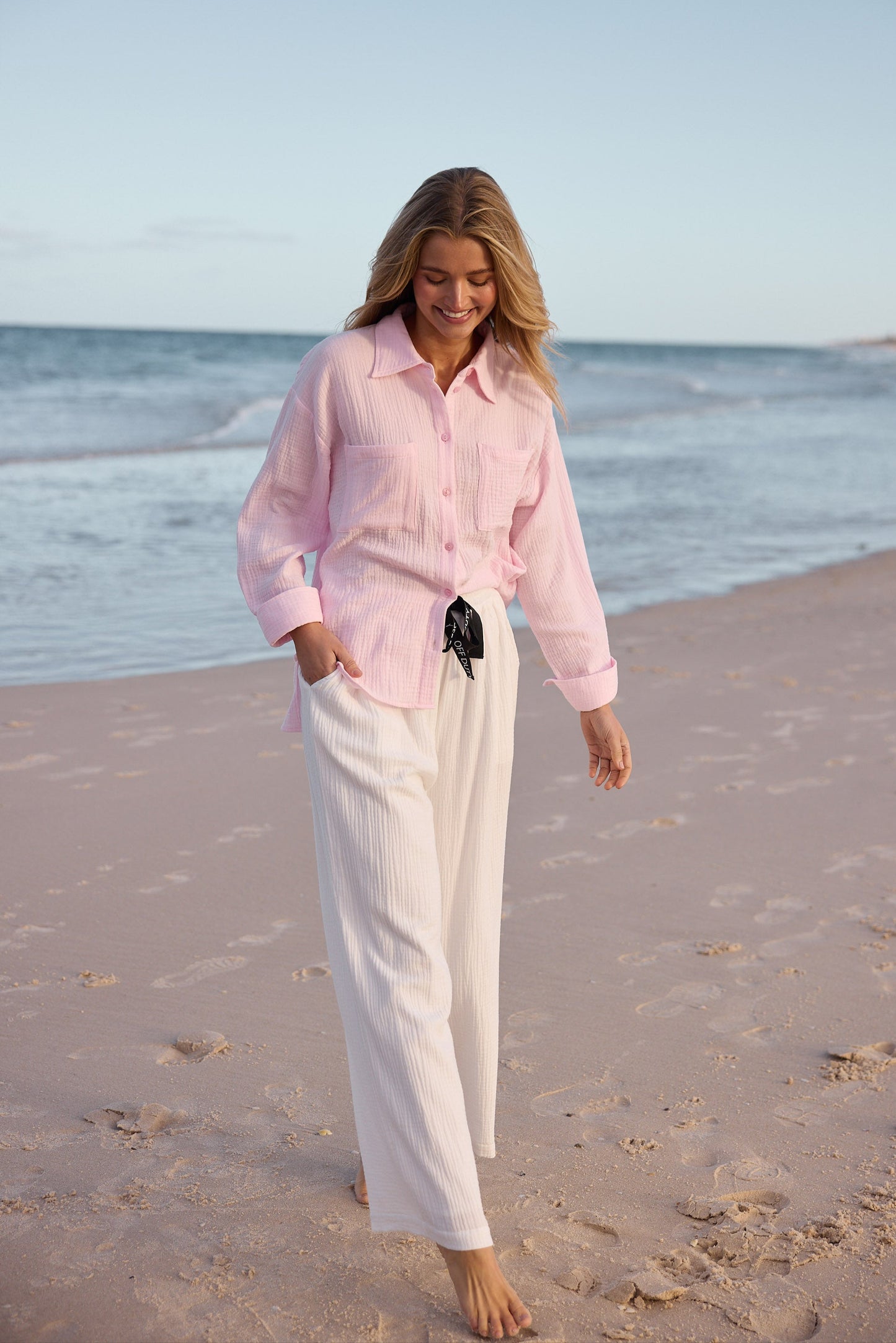 Woman in a pink shirt and white pants walking on a beach.