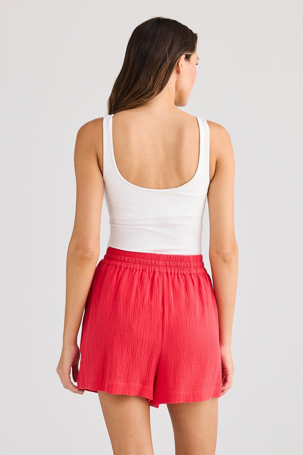 Woman wearing a white tank top and red shorts on a plain background