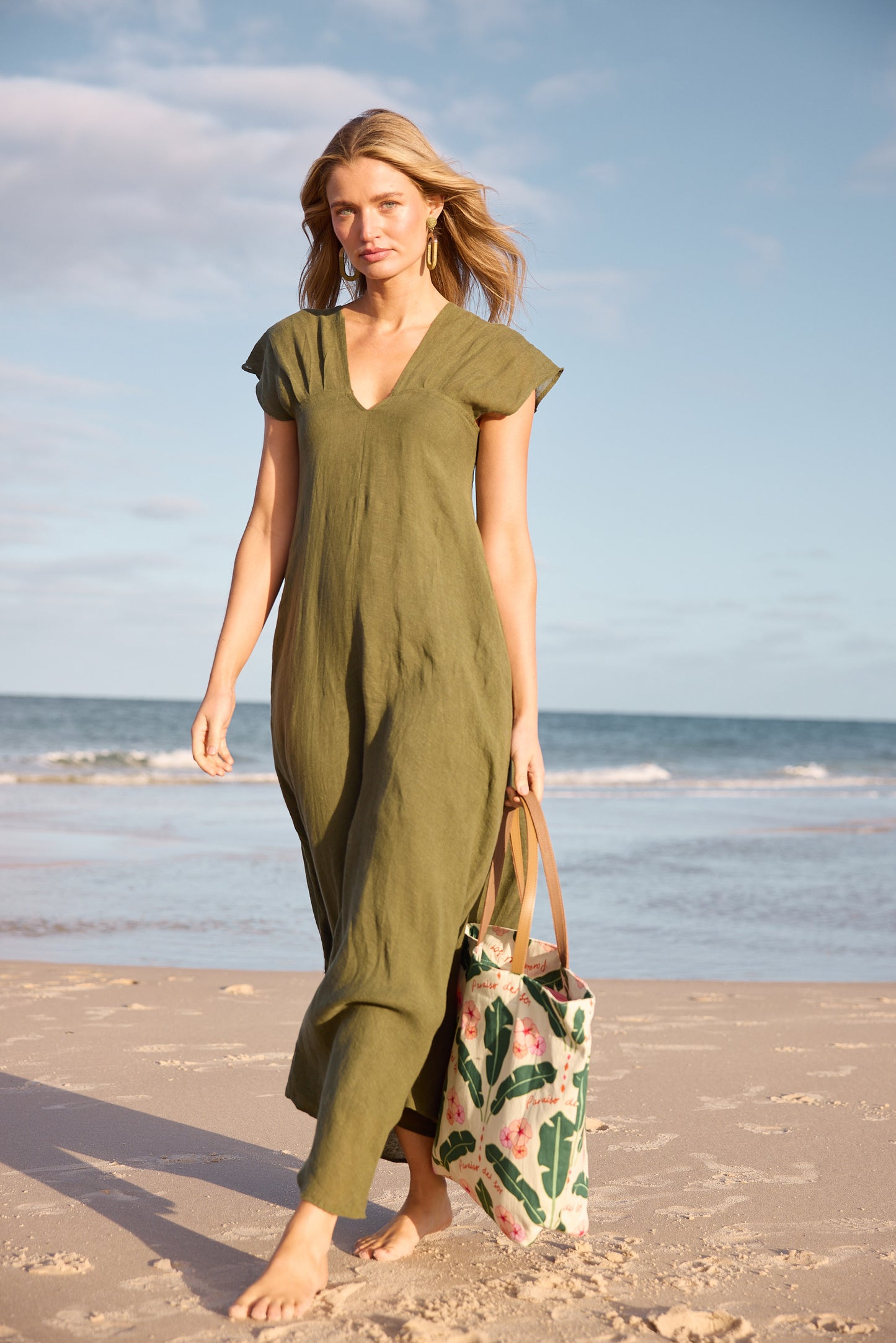Woman in a green dress holding a floral bag on a beach