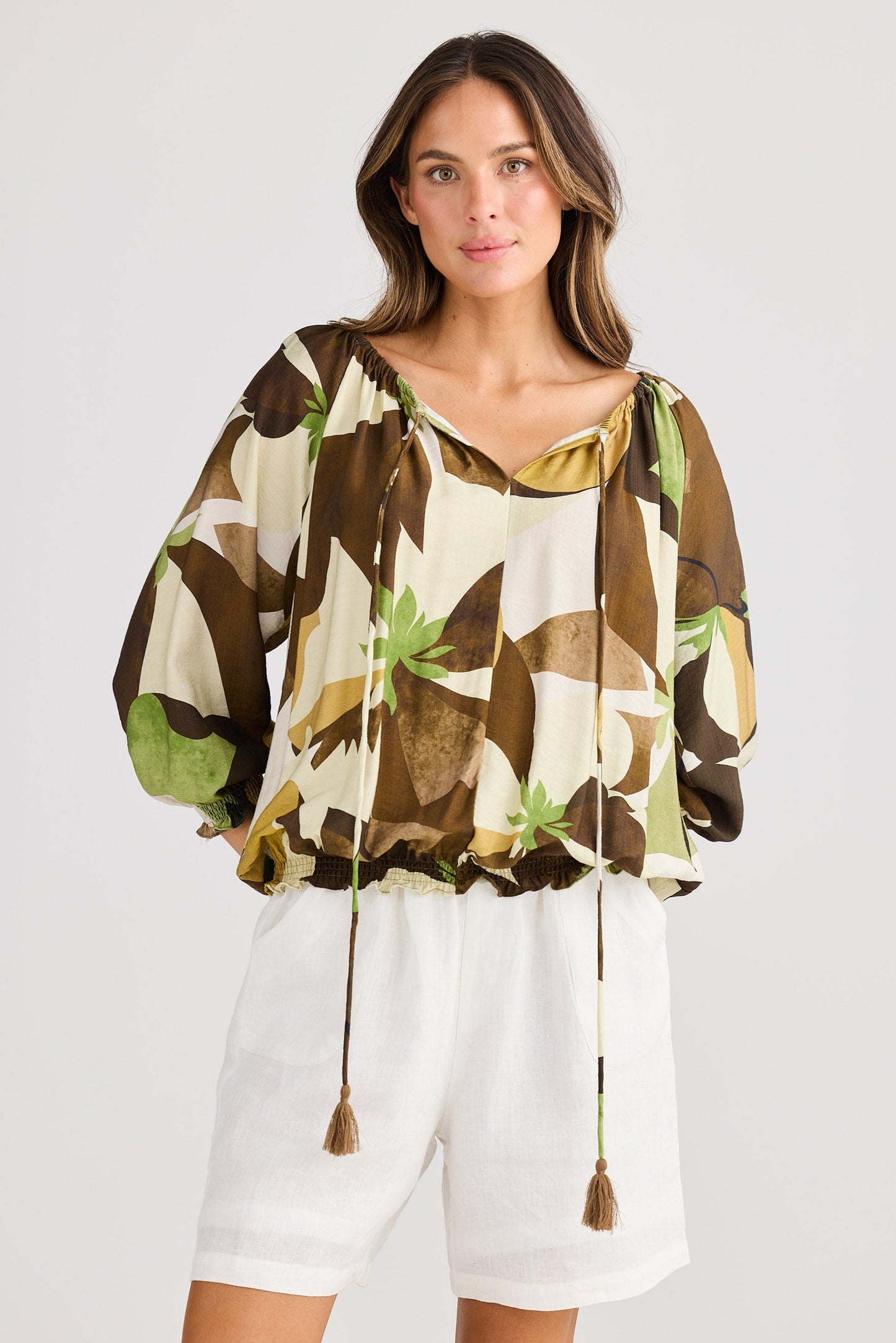 Woman wearing a floral blouse and white shorts on a plain background