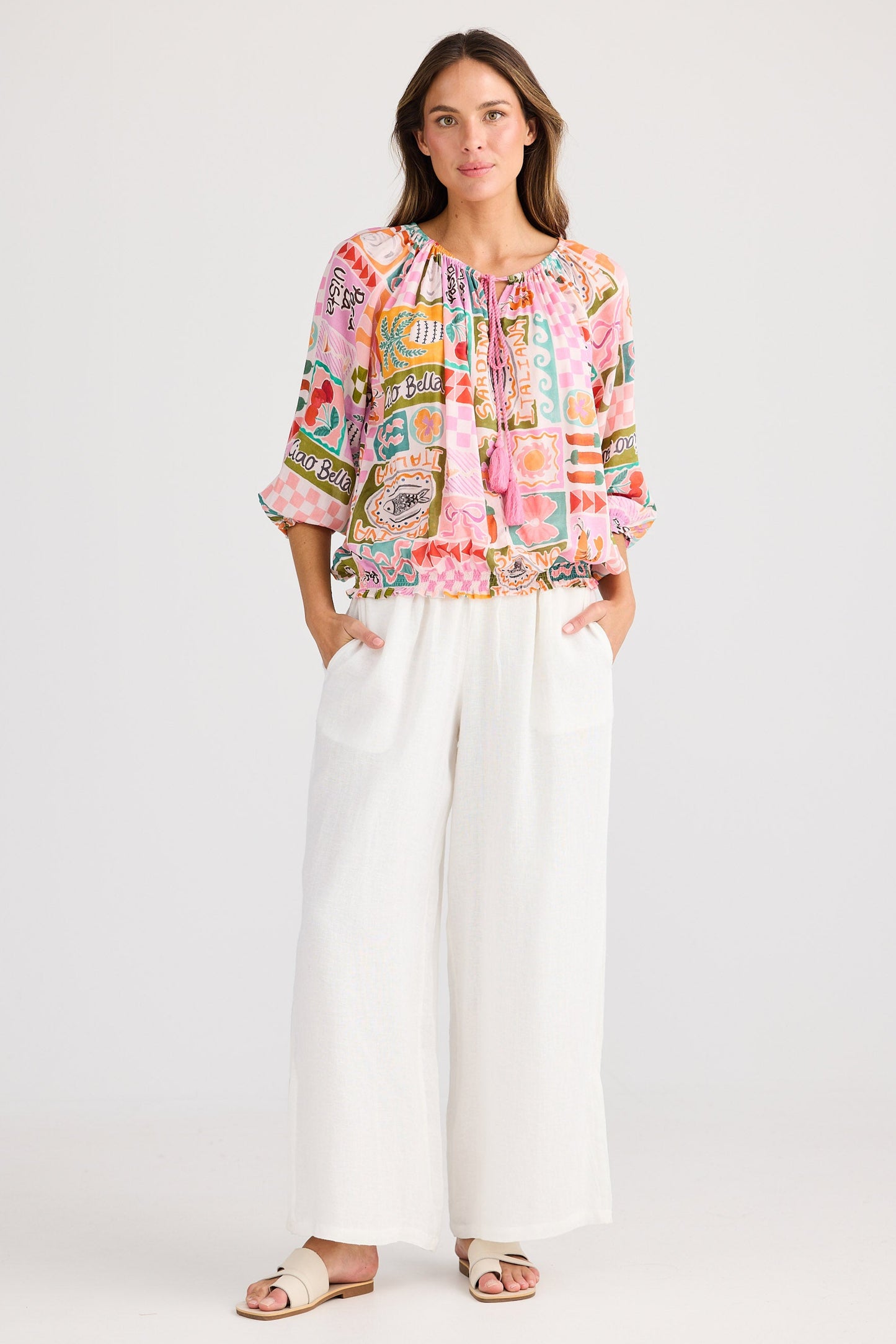 Woman wearing a colorful patterned top and white pants on a white background
