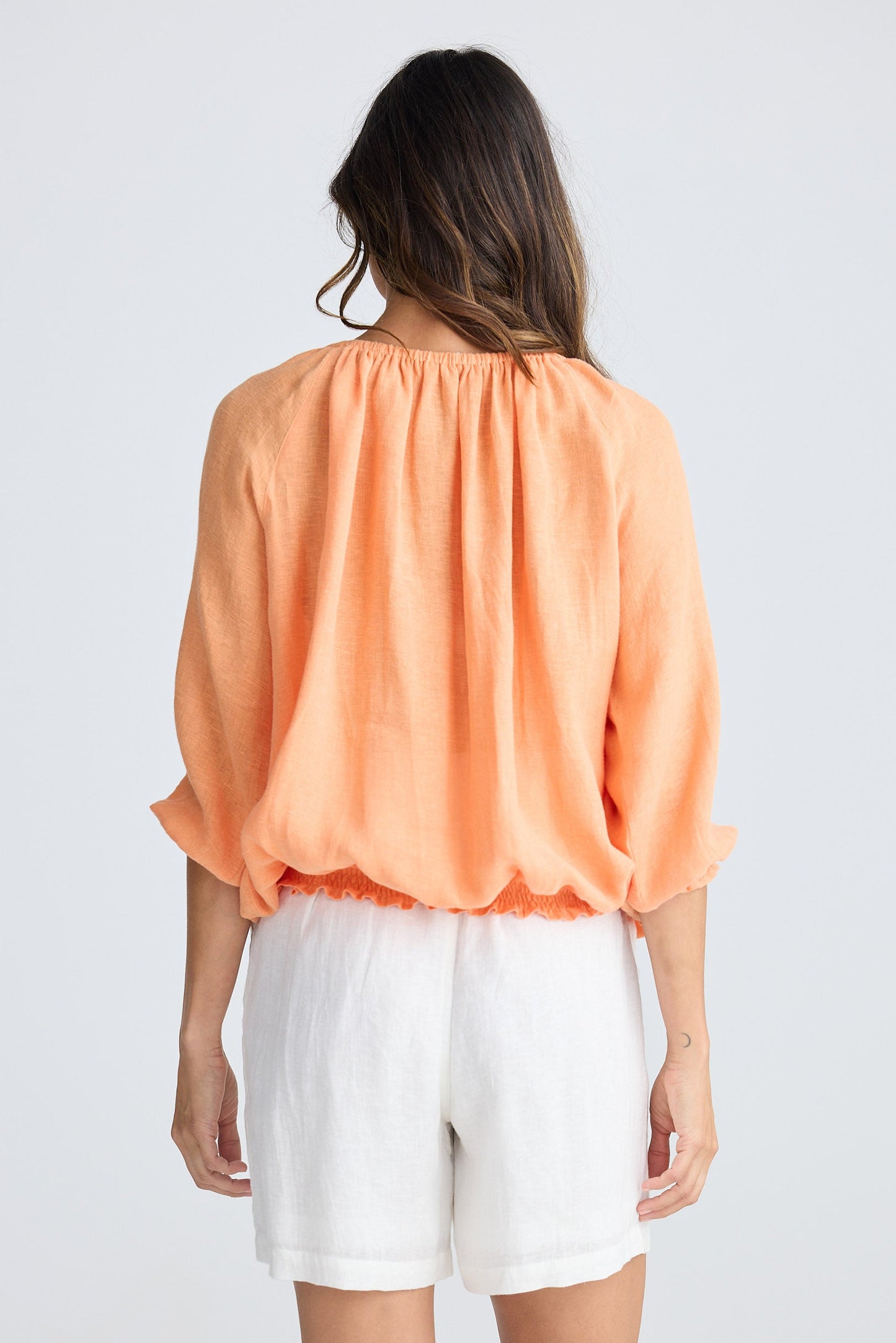 Woman wearing an orange blouse and white shorts on a plain background