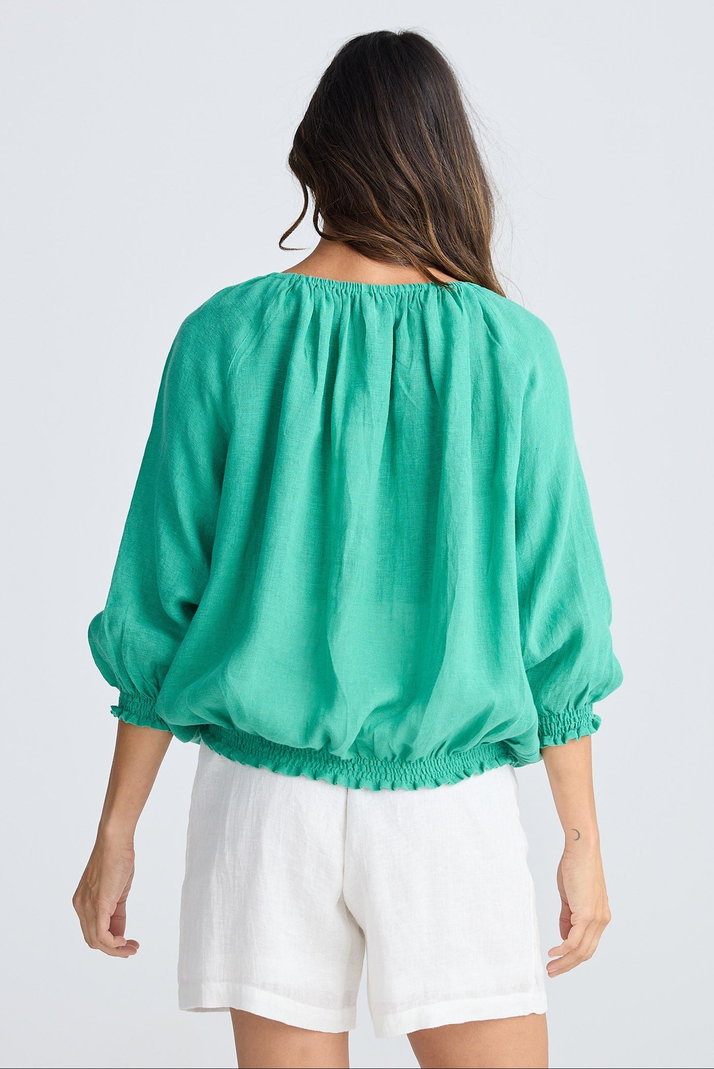 Woman wearing a green blouse and white shorts on a light gray background