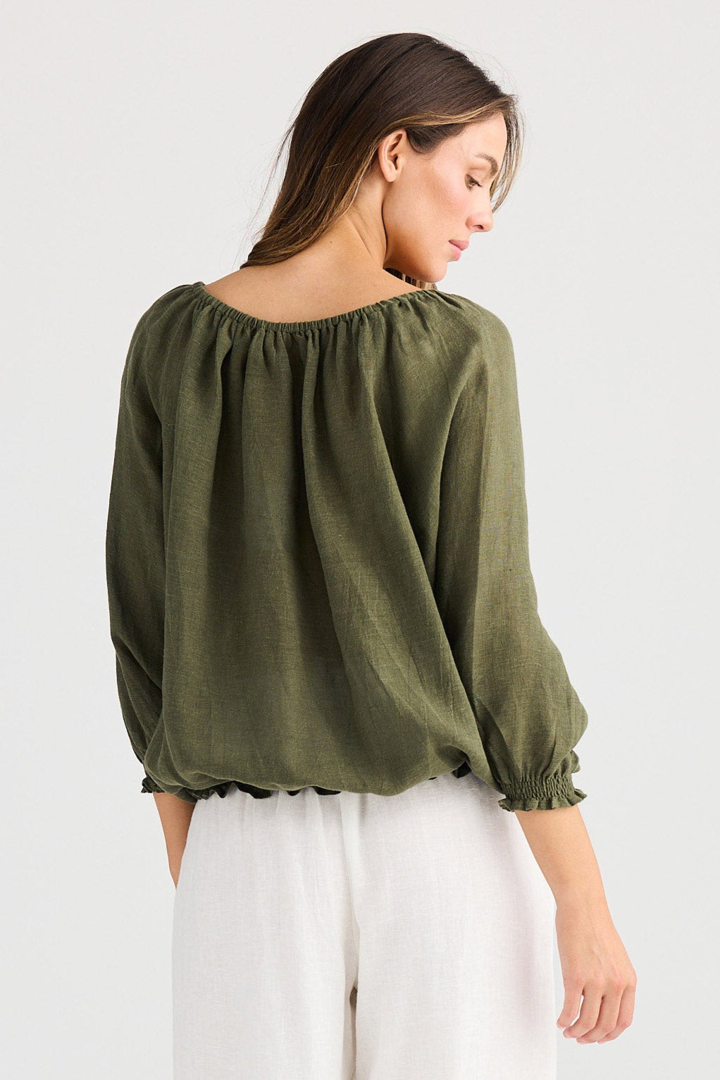 Woman wearing an olive green blouse and white pants on a white background