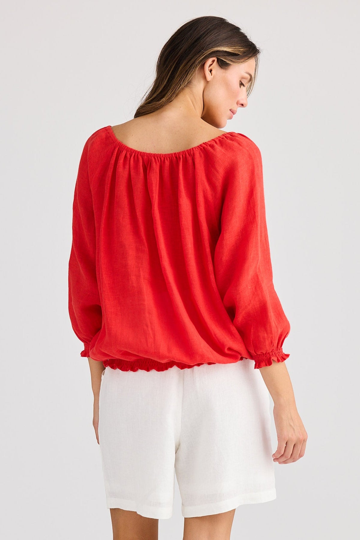 Woman wearing a red blouse and white shorts on a plain background