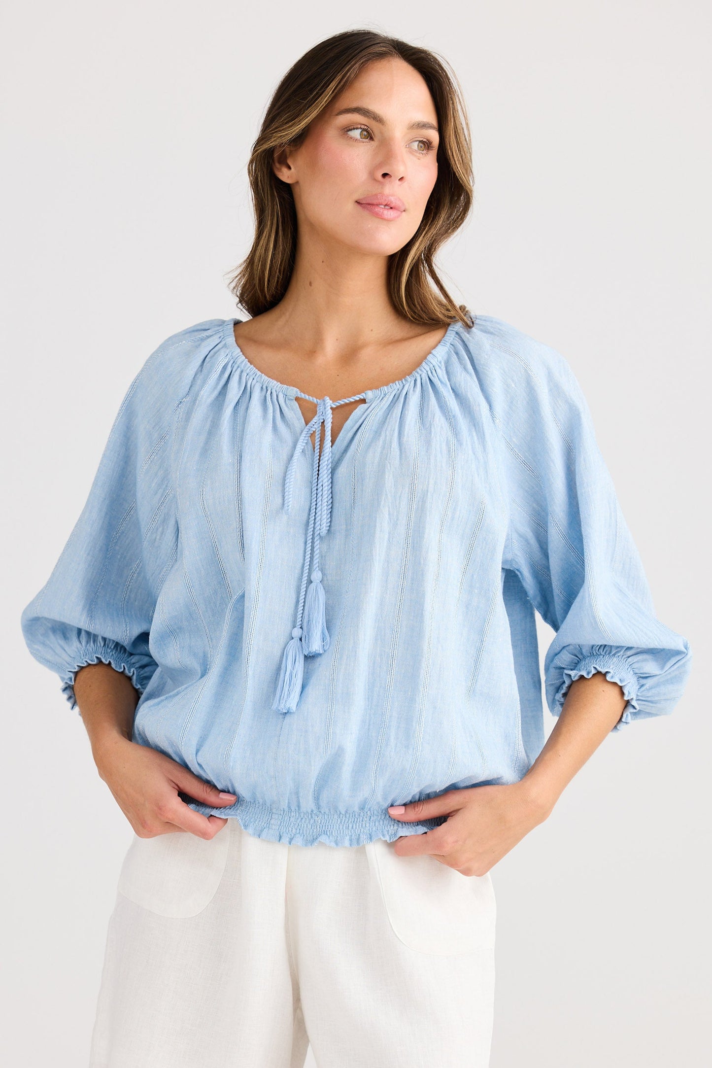 Woman wearing a light blue blouse and white shorts on a plain background