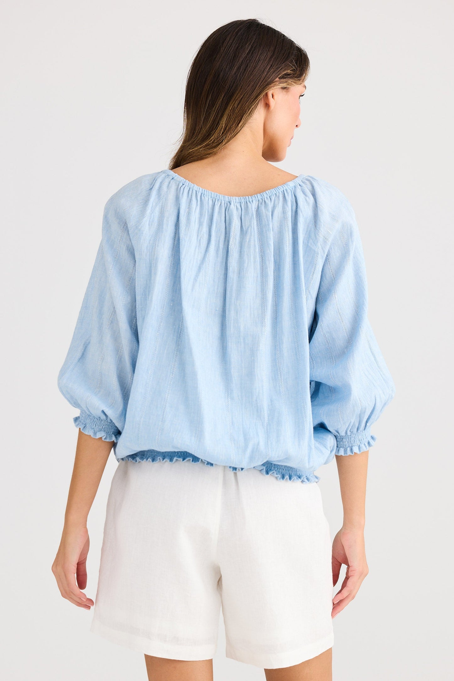 Woman wearing a light blue blouse and white shorts on a plain background
