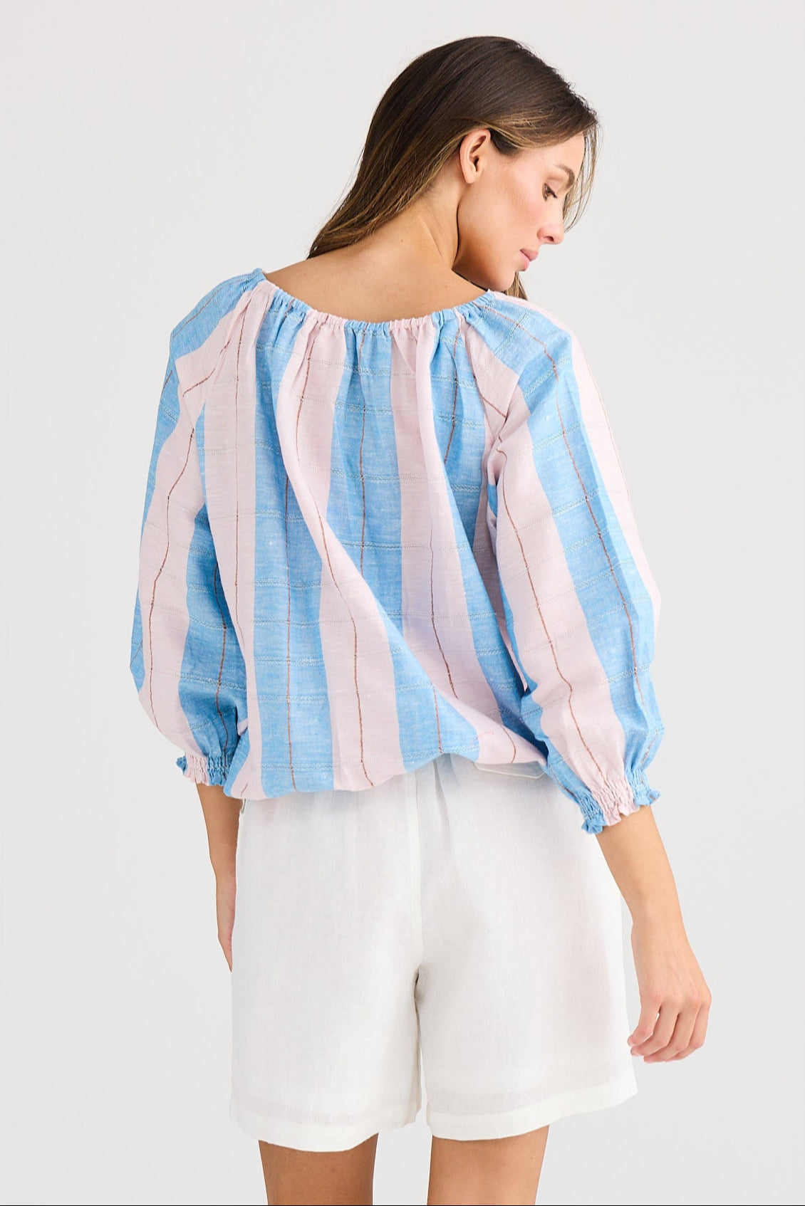 Woman wearing a striped shirt and white shorts on a plain background
