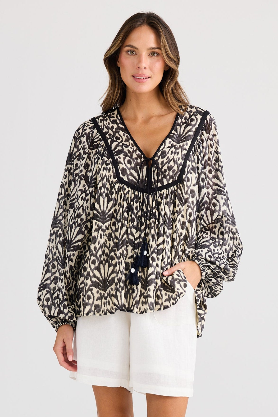 Woman wearing a patterned blouse and white shorts on a plain background