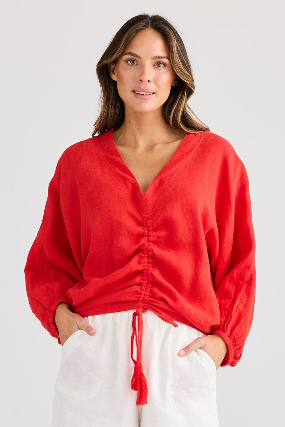 Woman wearing a red blouse and white shorts on a light gray background