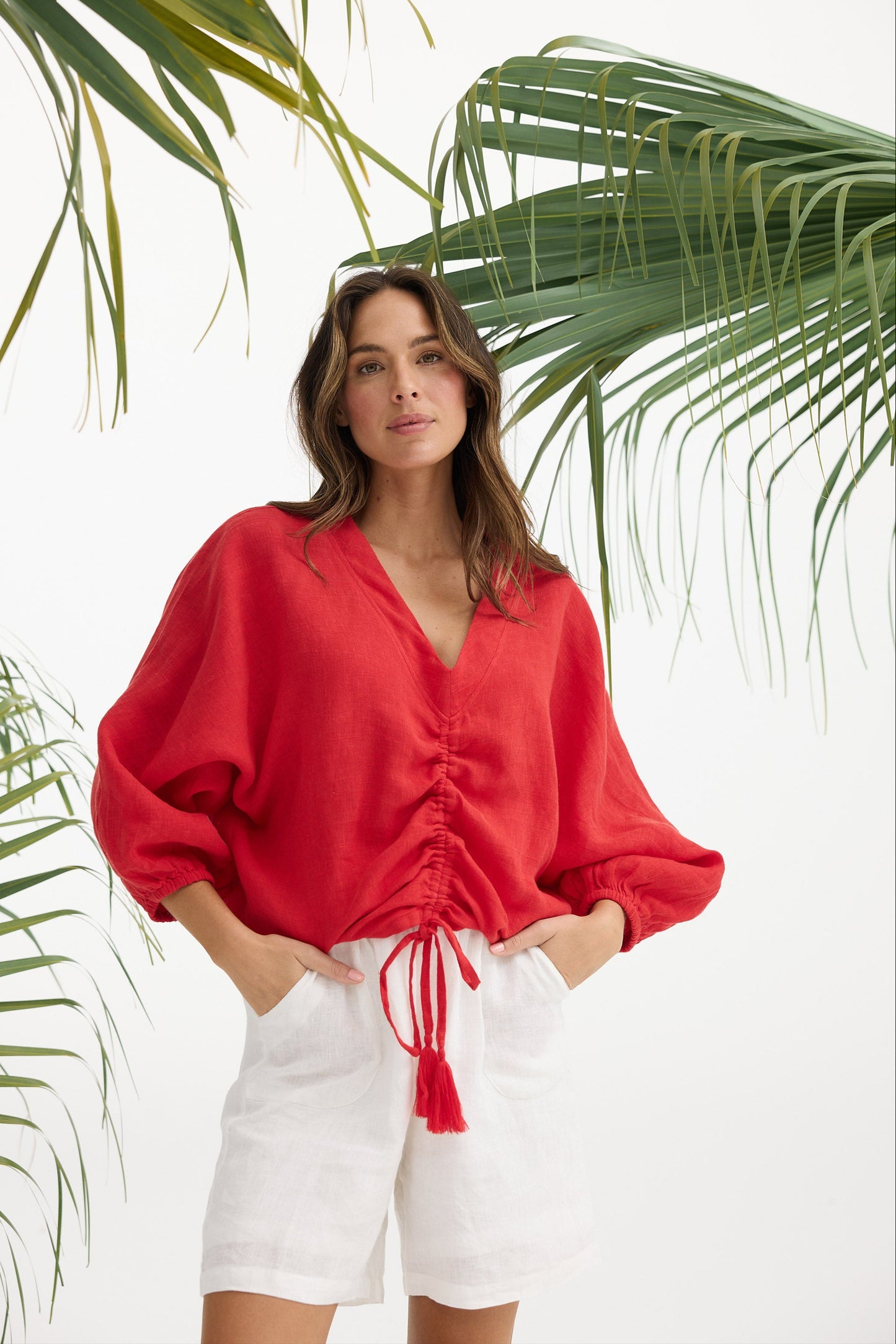Woman wearing a red blouse and white shorts with green leaves in the background