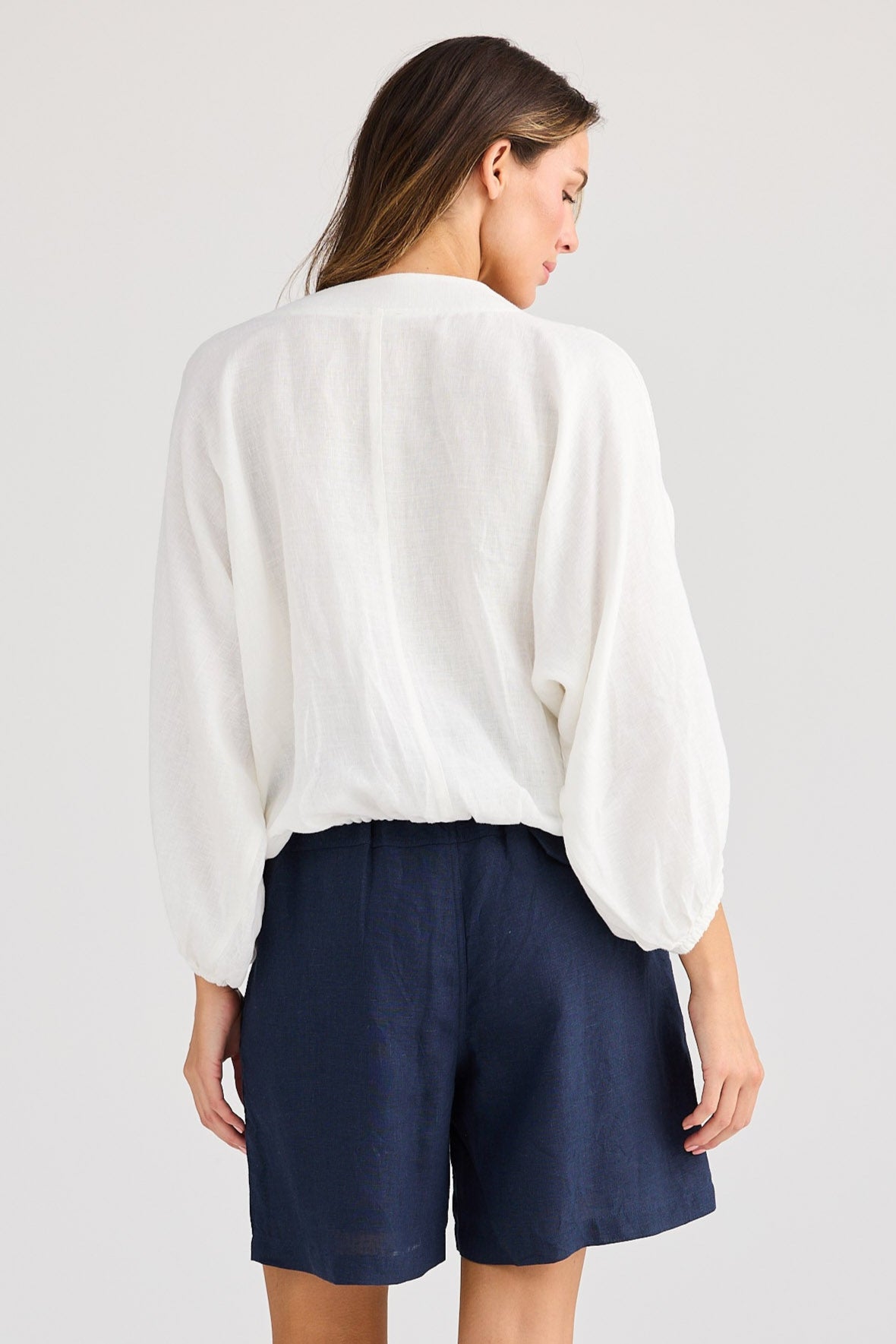 Woman wearing a white blouse and navy shorts on a plain background