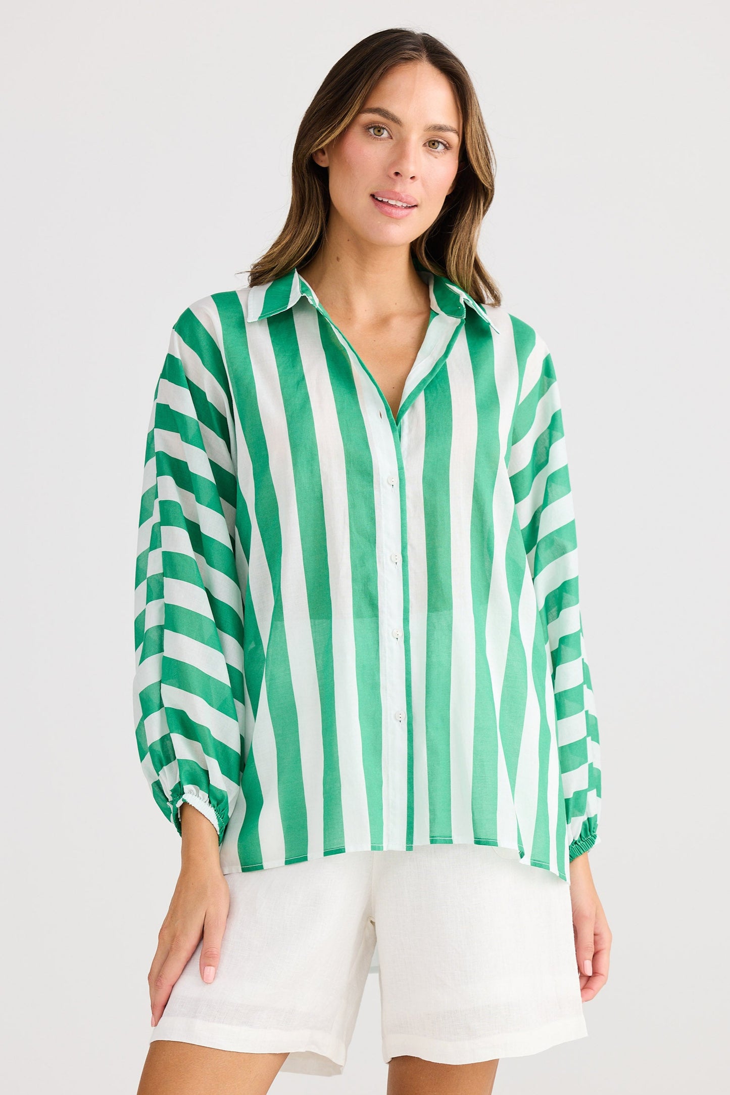 Woman wearing a green and white striped shirt with white shorts on a light gray background