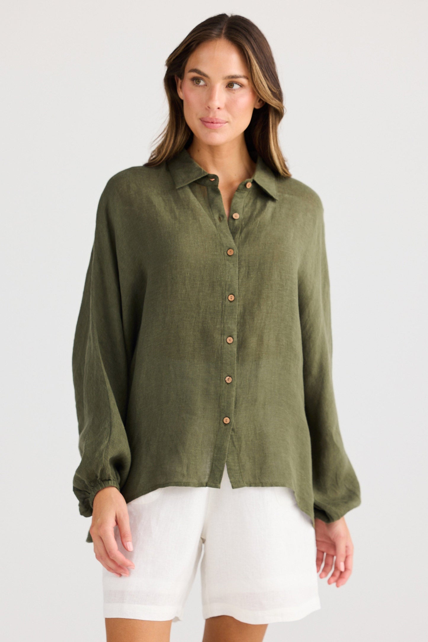 Woman wearing an olive green button-up shirt and white shorts on a light gray background
