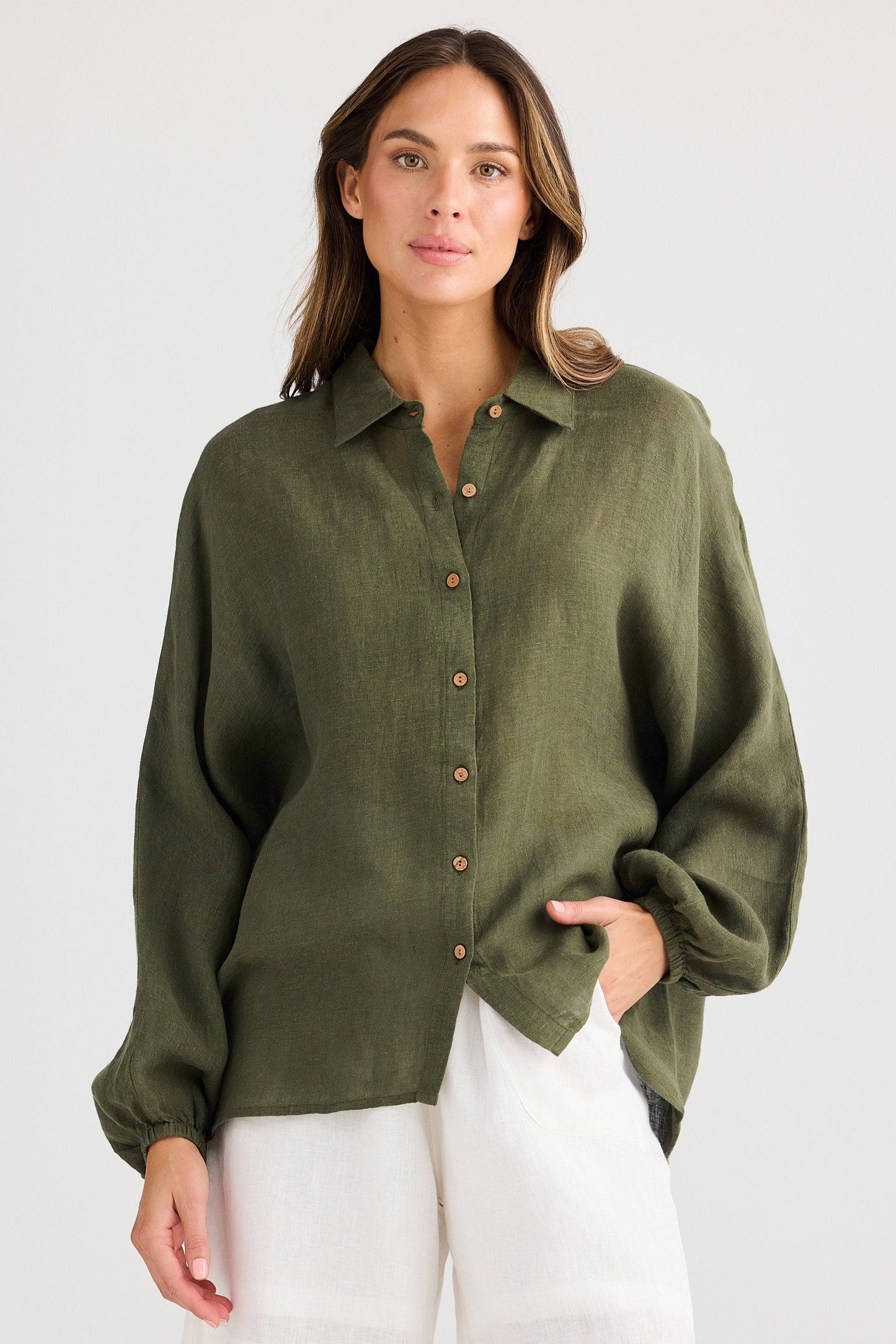 Woman wearing an olive green button-up shirt and white shorts on a plain background