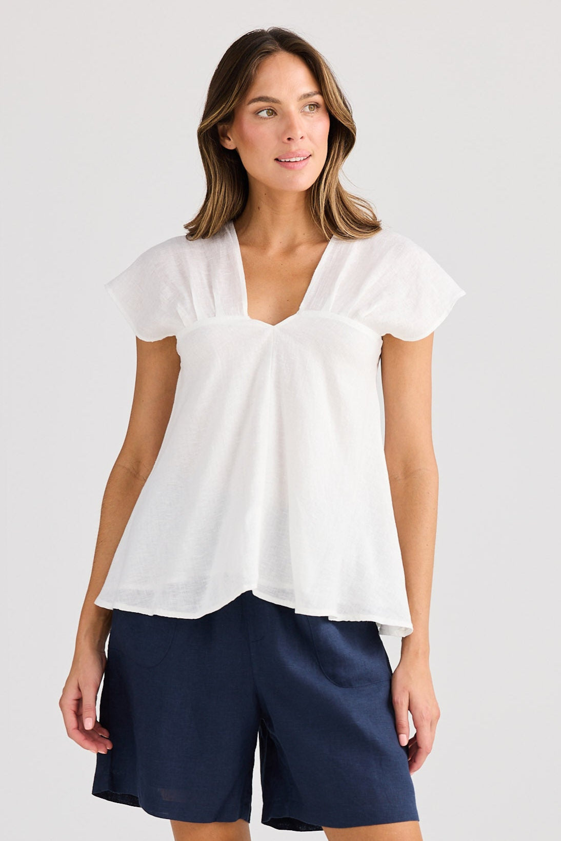 Woman wearing a white blouse and navy shorts on a light gray background