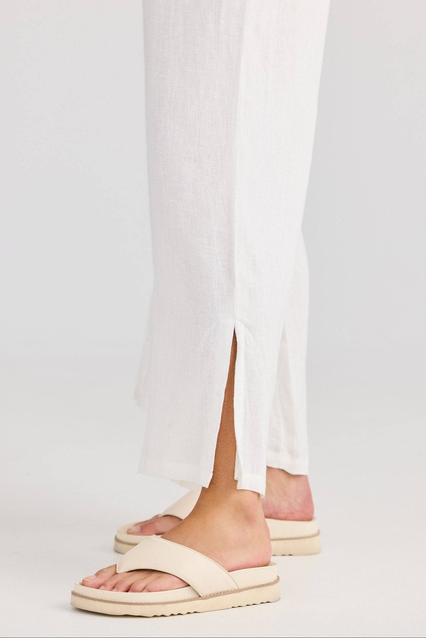 Beige sandals worn with white pants on a light gray background
