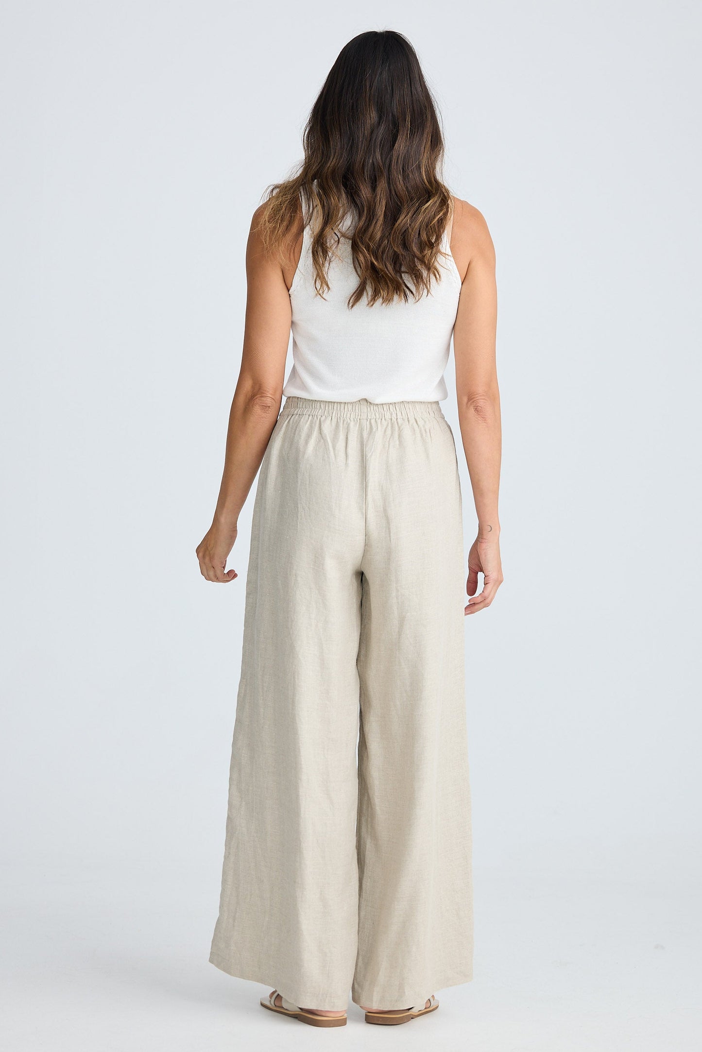 Woman wearing a white sleeveless top and beige wide-leg pants on a white background