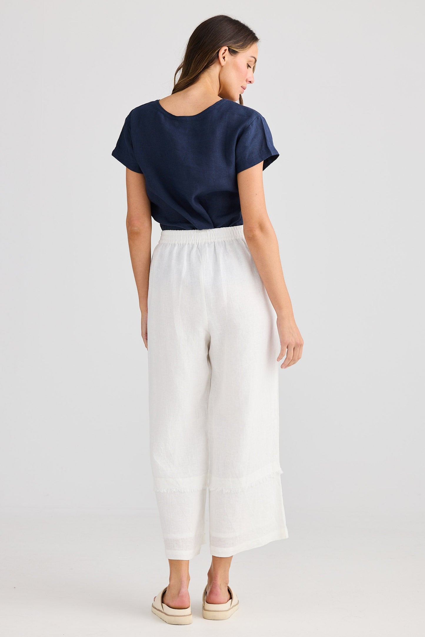Woman wearing a navy top and white pants on a light gray background