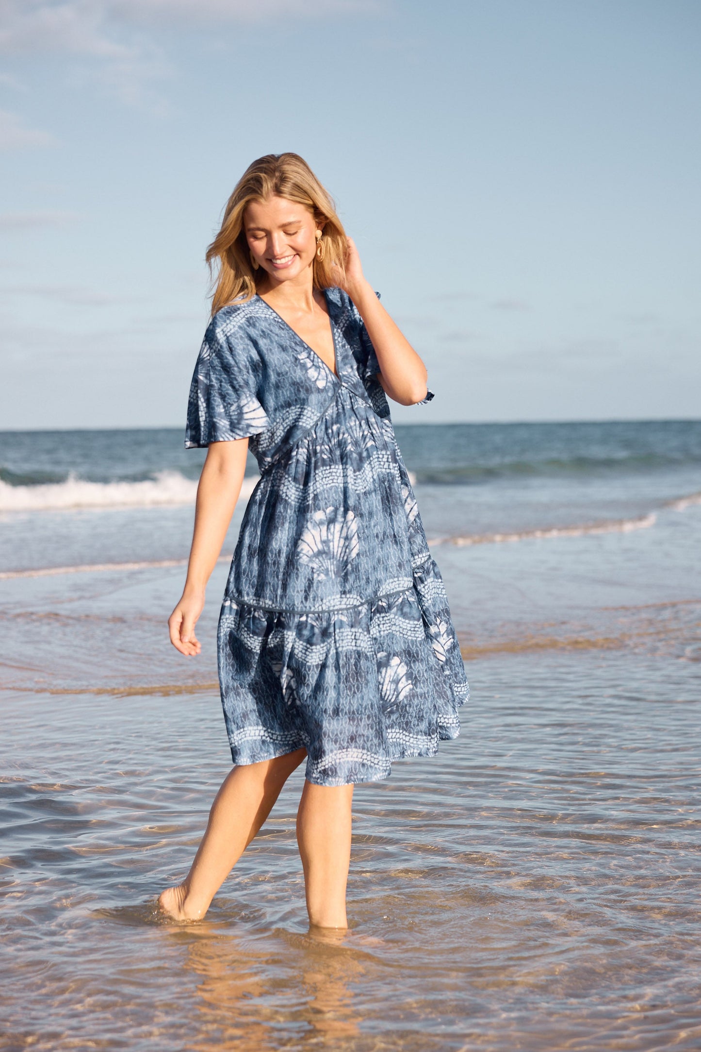 Woman in a blue dress walking on a beach with ocean waves in the background
