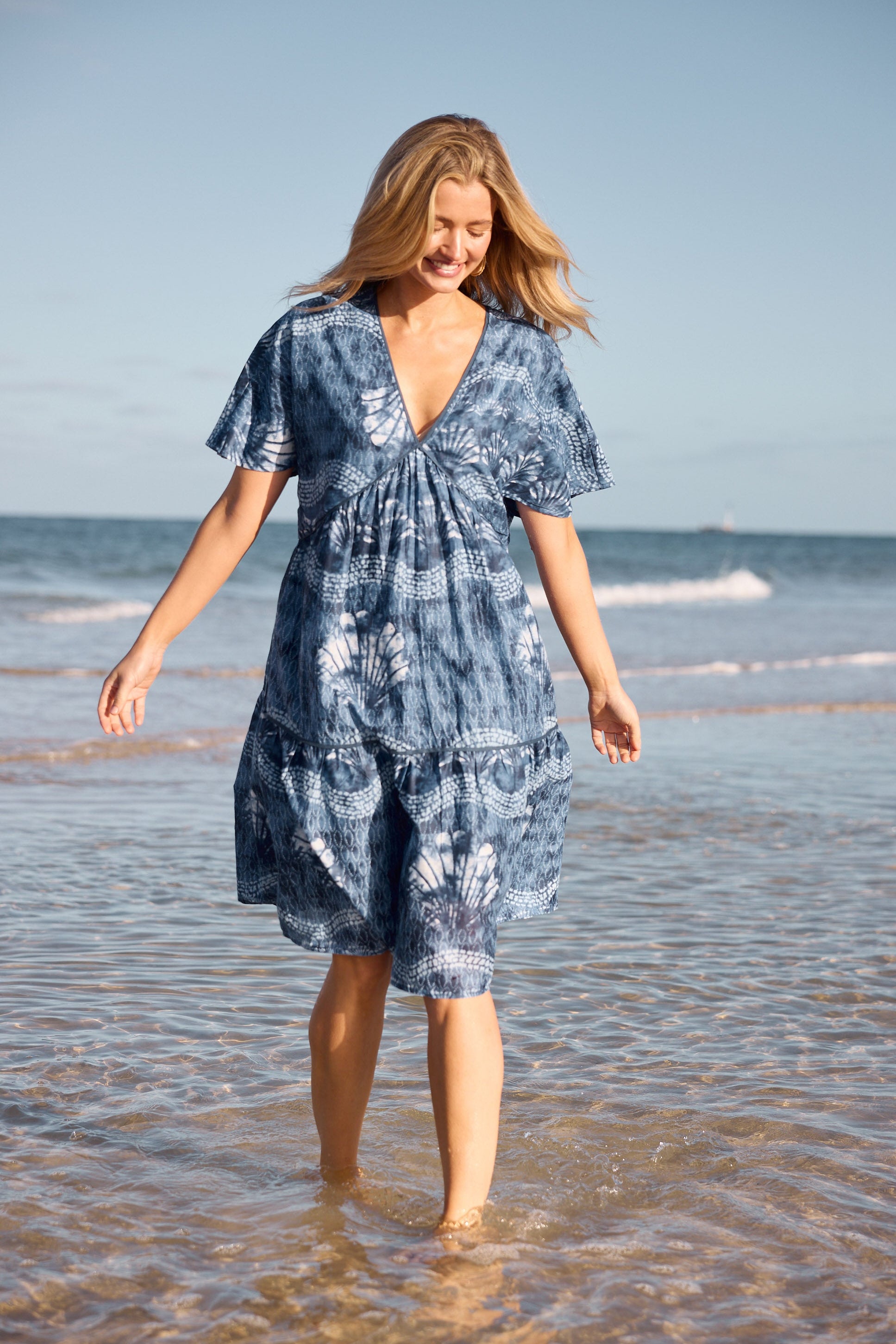 Woman in a blue tie-dye dress walking on a beach