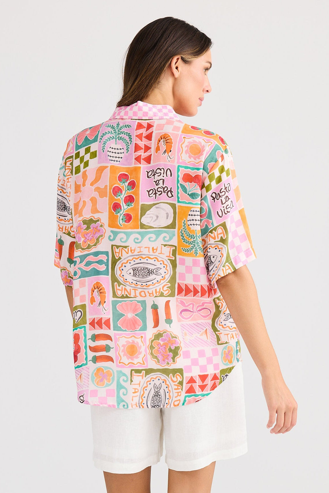 Woman wearing a colorful patterned shirt and white shorts on a plain background