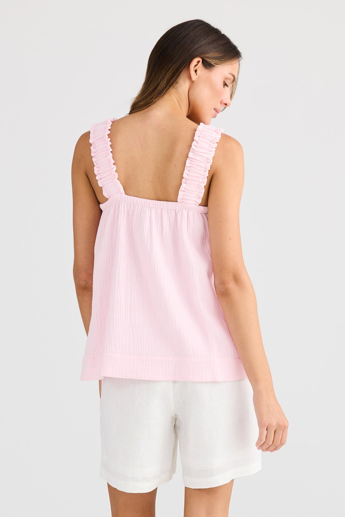 Woman wearing a pink sleeveless top and white shorts on a light gray background