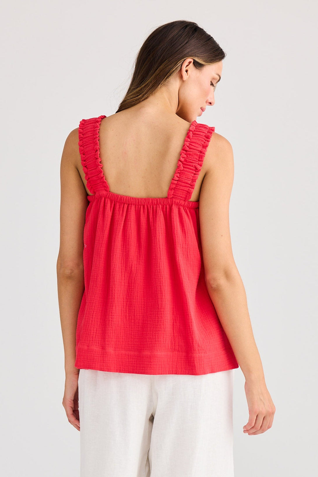 Woman wearing a red sleeveless top and white pants on a plain background