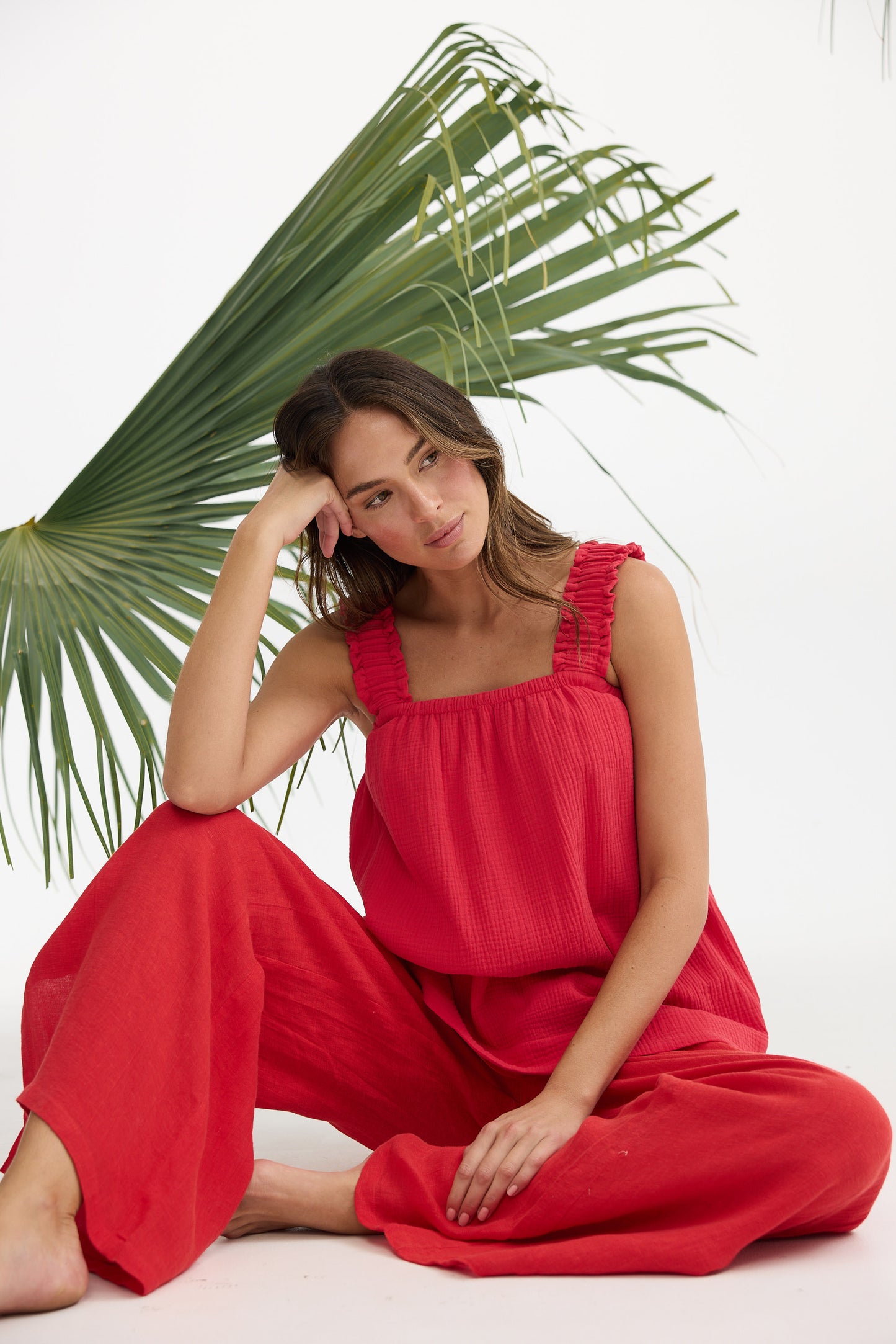 Woman in a red outfit sitting against a white background with a palm leaf.