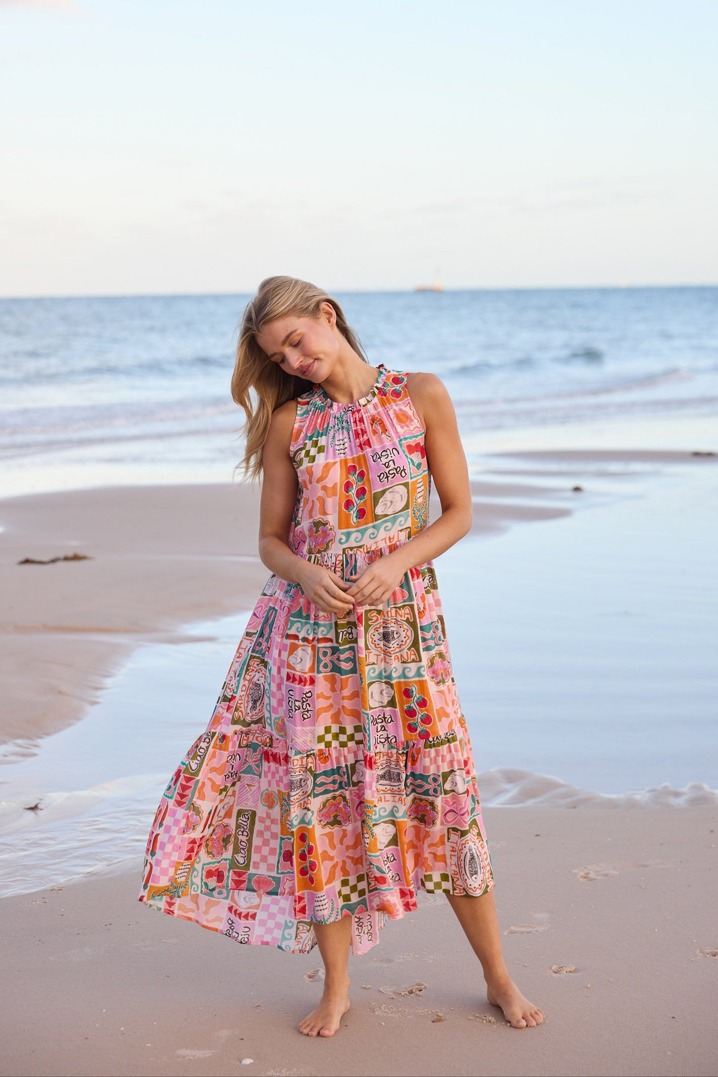 Woman in a colorful dress standing on a beach with ocean waves in the background