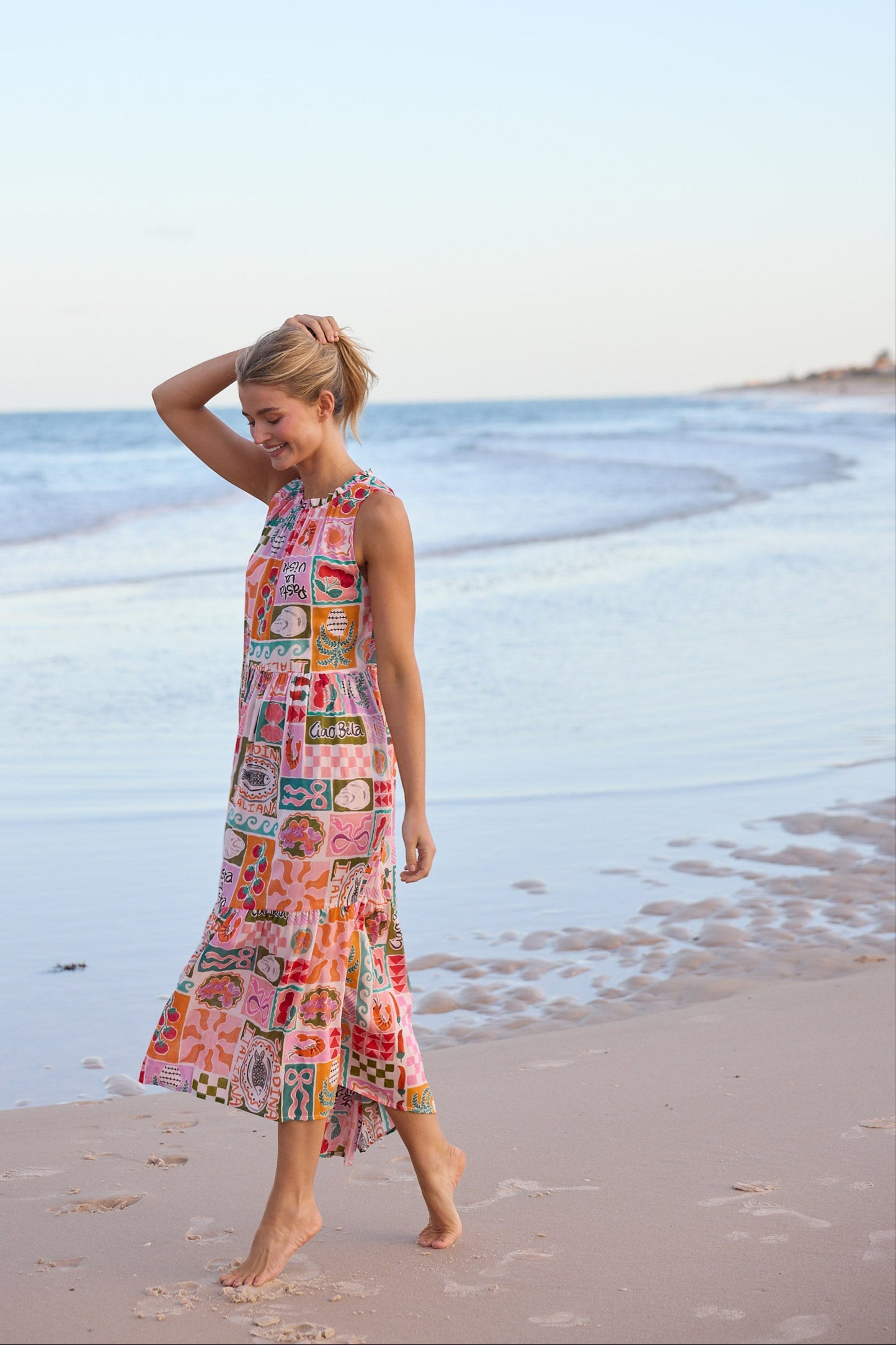 Woman in a colorful dress standing on a beach with ocean waves in the background