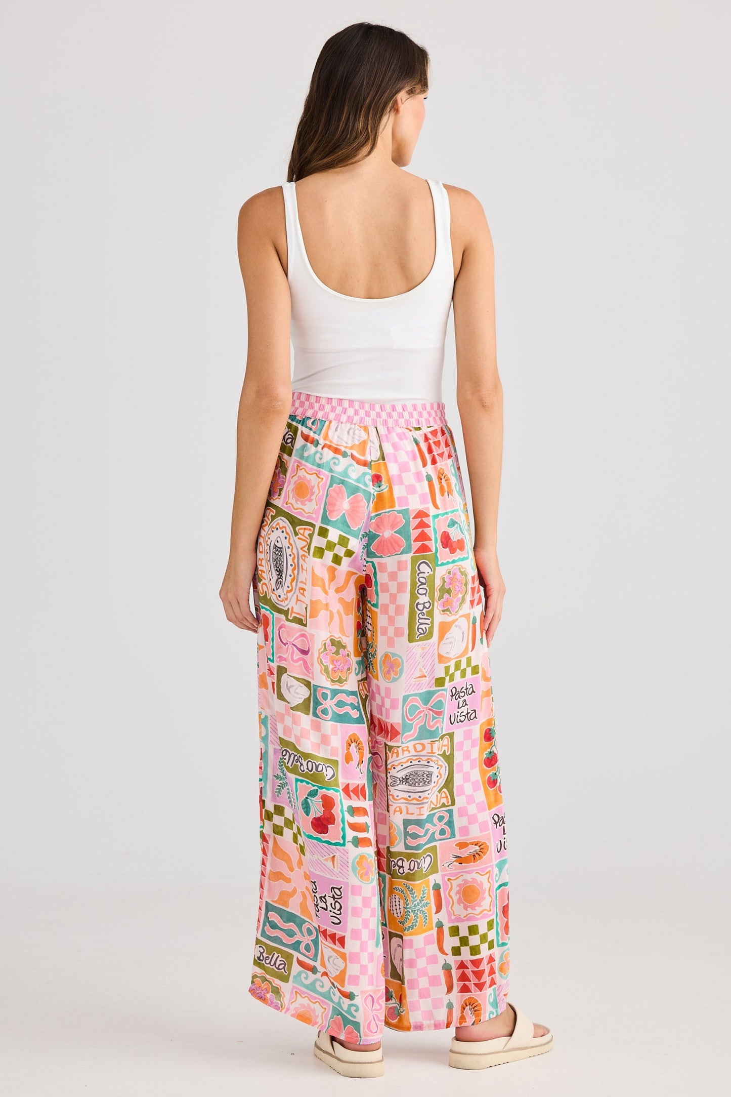 Woman wearing a white tank top and colorful patterned pants on a light gray background