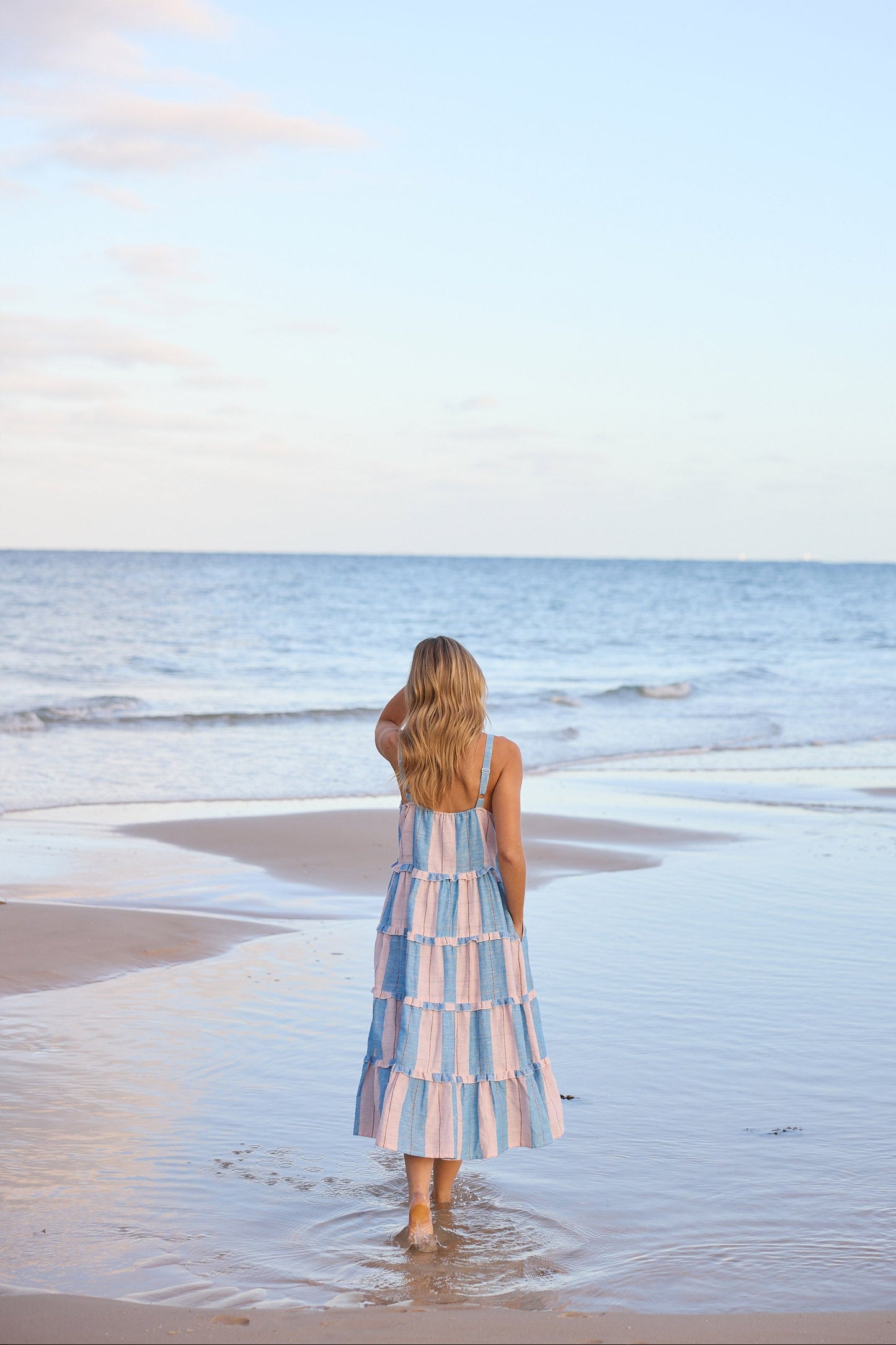 Woman in a striped dress standing on a beach looking at the ocean.
