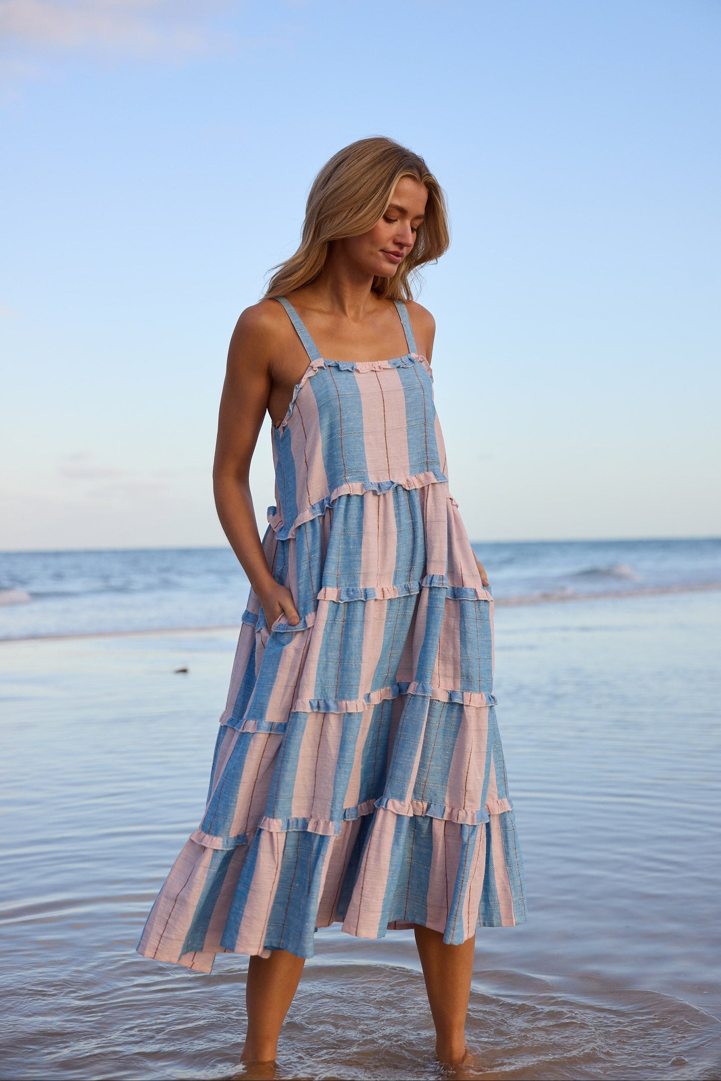 Woman in a striped dress standing on a beach with ocean in the background